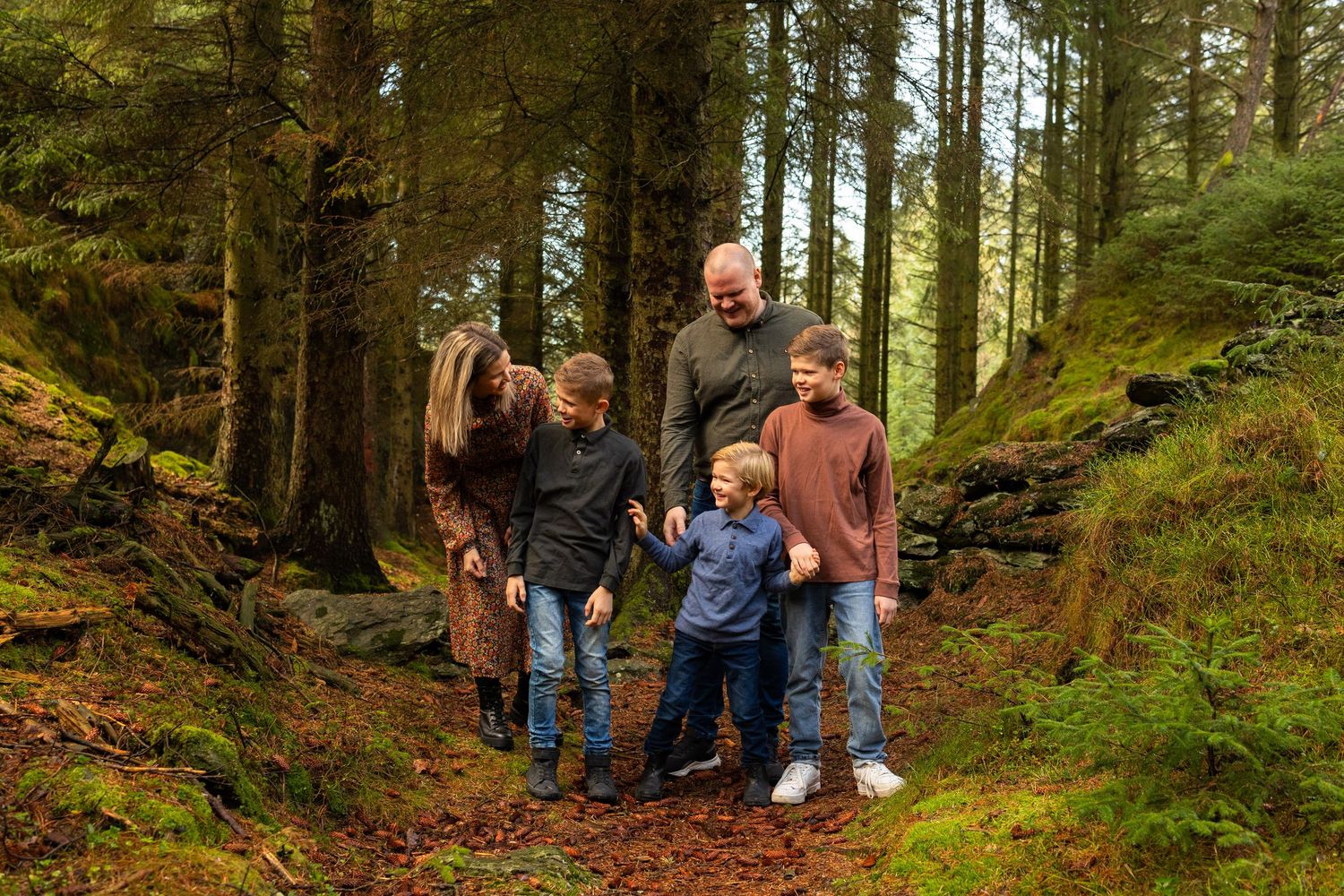 En familie som nyter høsten i skogen med nydelige jordtoner og ler og tøyser og ser lykkelige ut