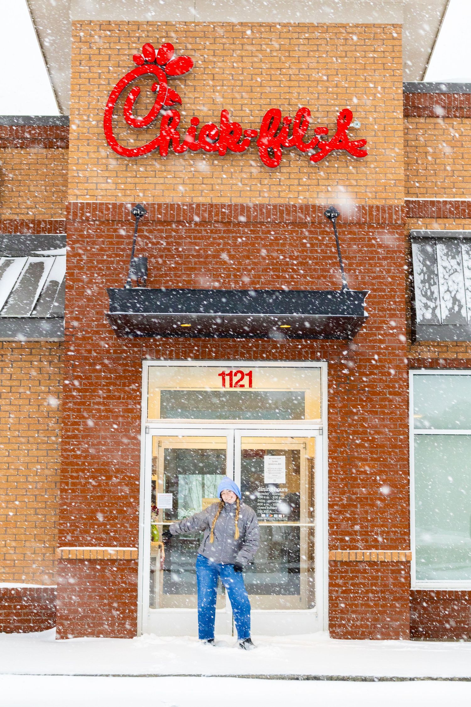 People walking outside a Chick-fil-A restaurant during a heavy snowstorm with red signage visible on brick building.