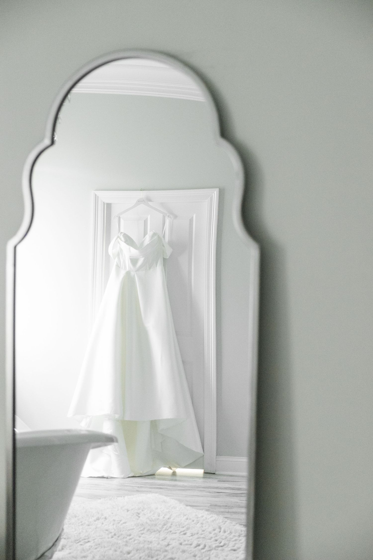 A series of arched mirrors reflect a minimalist white bedroom interior with soft lighting and bedding.