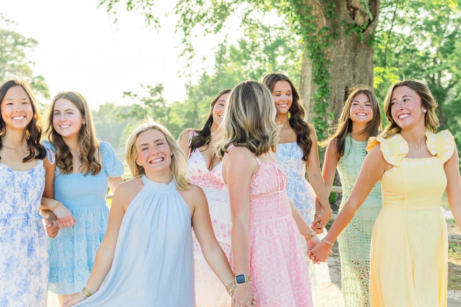 Group of women in pastel-colored dresses smile and pose together outdoors in spring for a joyful photo session.