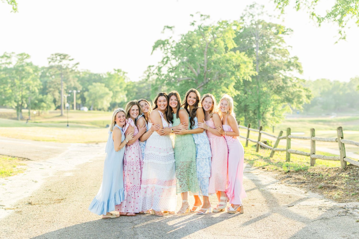 A group of people in pastel dresses pose together at an outdoor location during golden hour.
