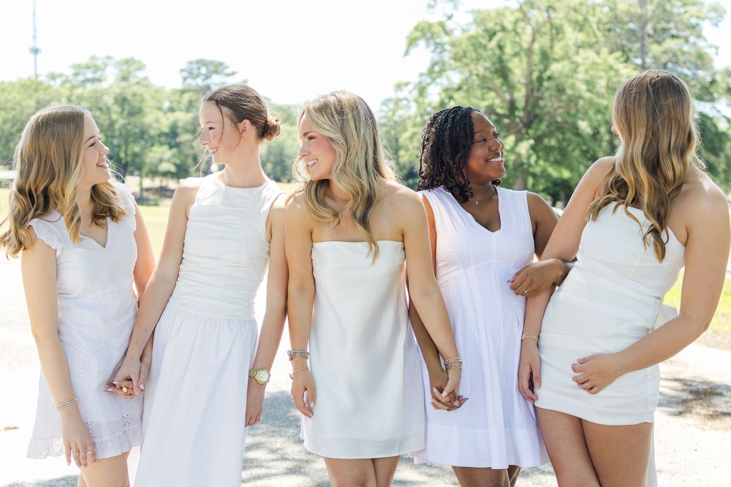 A row of people wearing white outfits stand side by side outdoors on a sunny day.