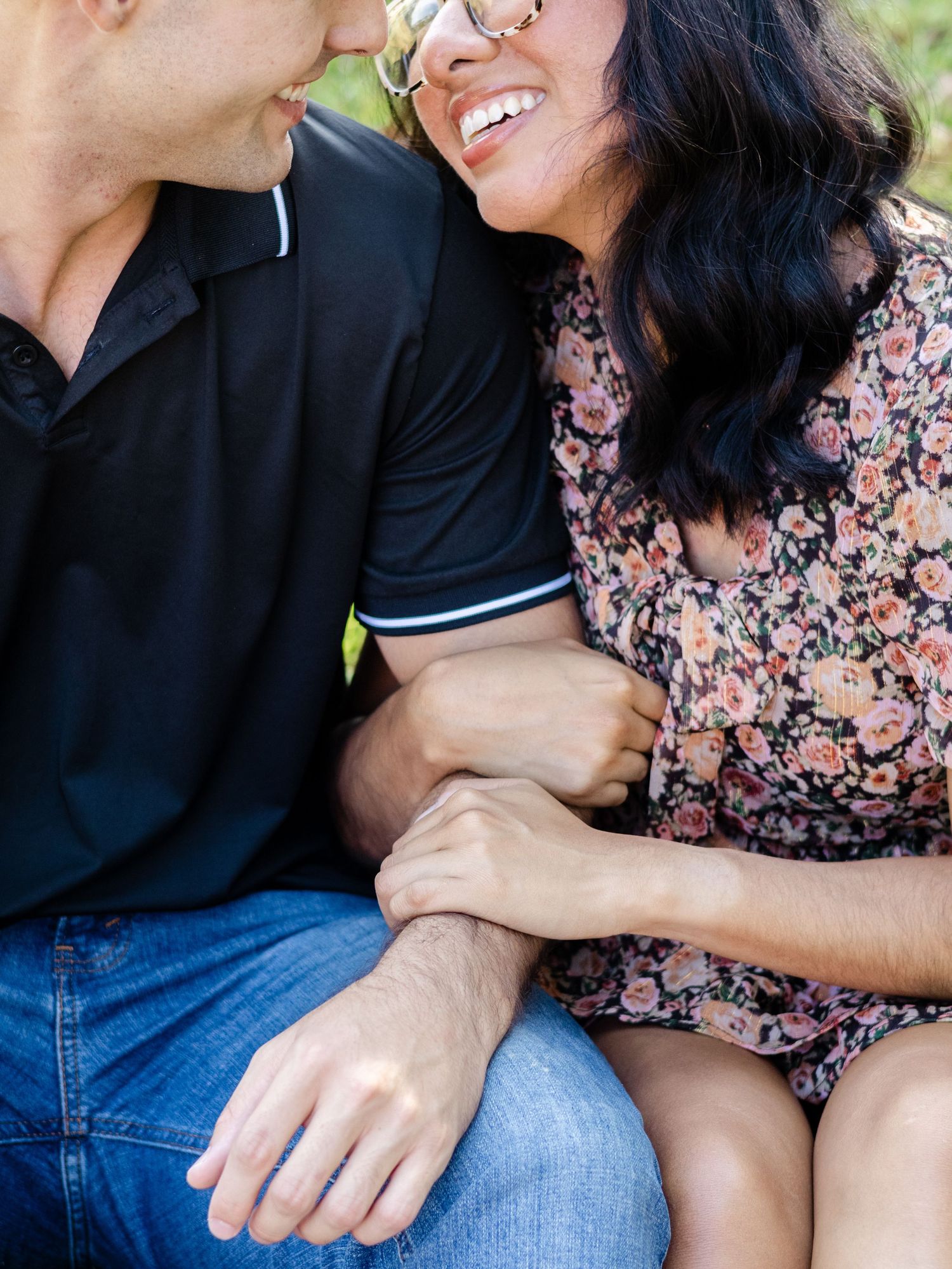 Cropped close-up shot showing a couple embracing and smiling while sitting together in casual attire outdoors.