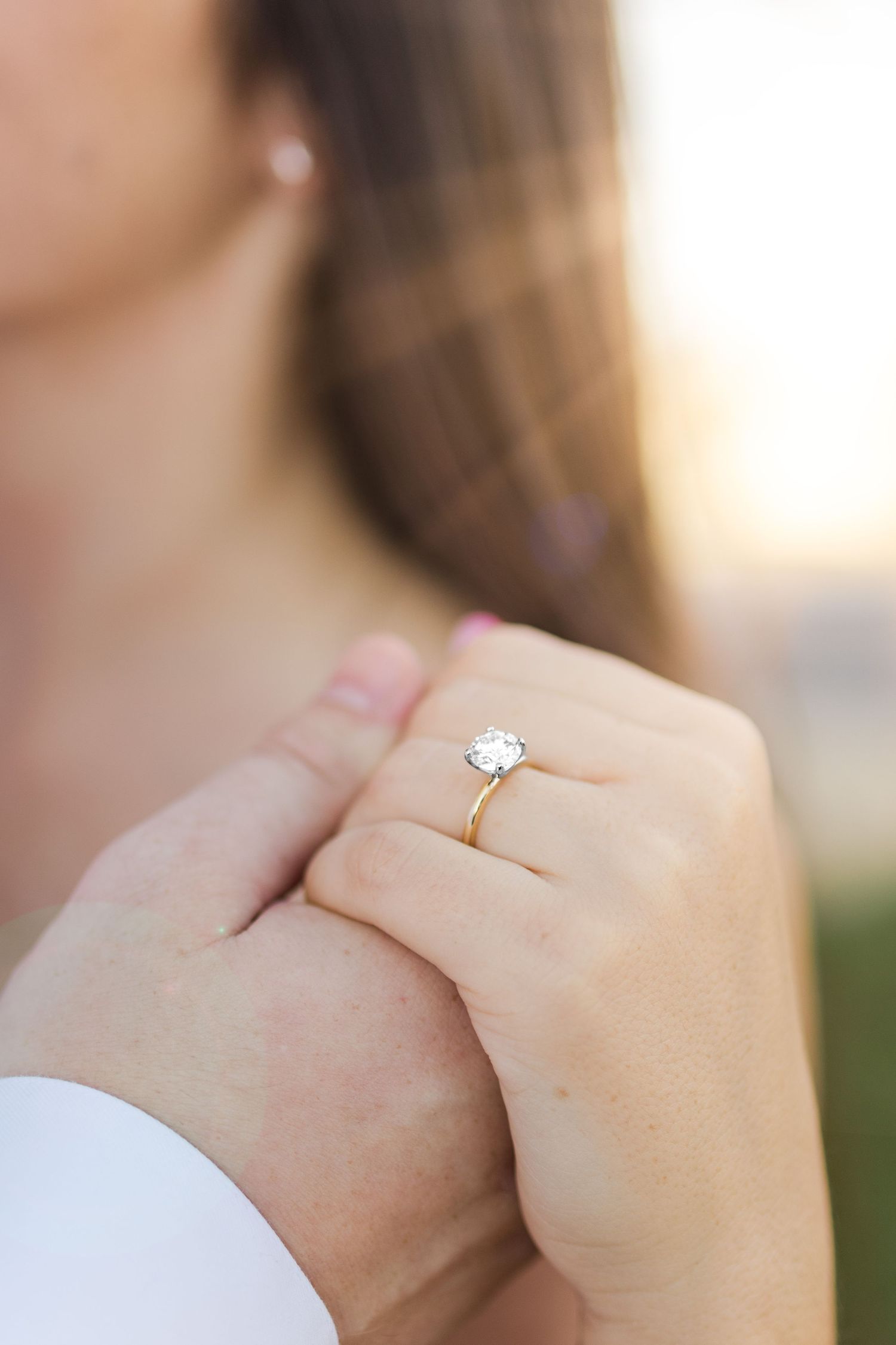 Close-up of hands holding together showing an elegant solitaire diamond engagement ring on a finger.