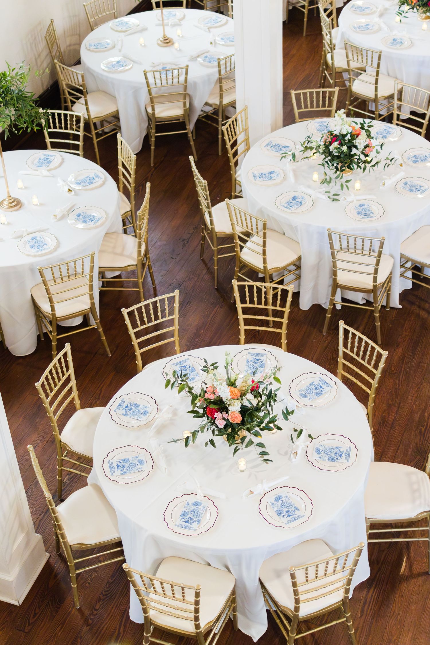 White tablecloths and elegant gold chiavari chairs set up for an elegant wedding reception with floral centerpieces.