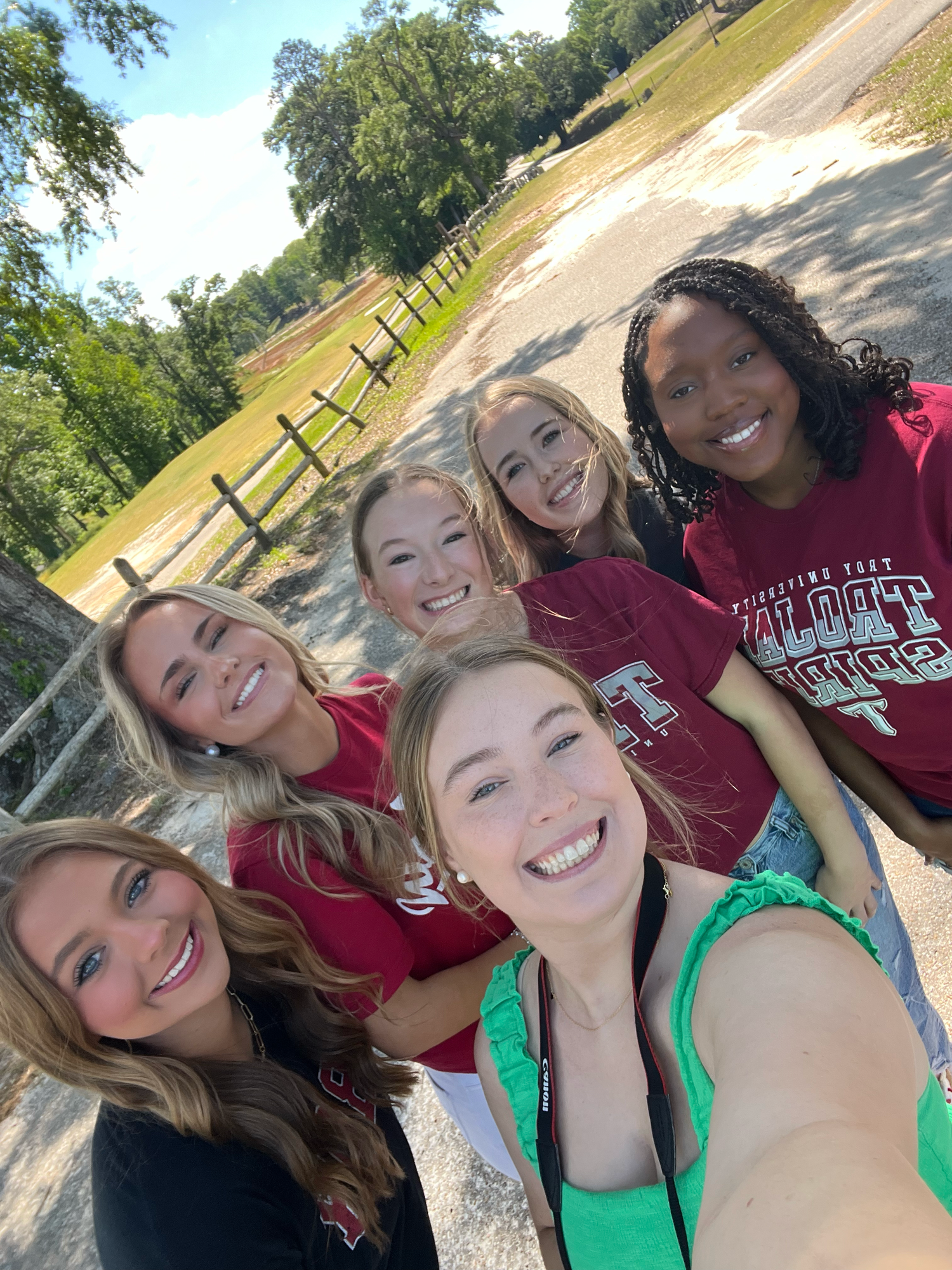 Group of friends wearing red school spirit shirts taking a cheerful selfie outdoors on a sunny day.