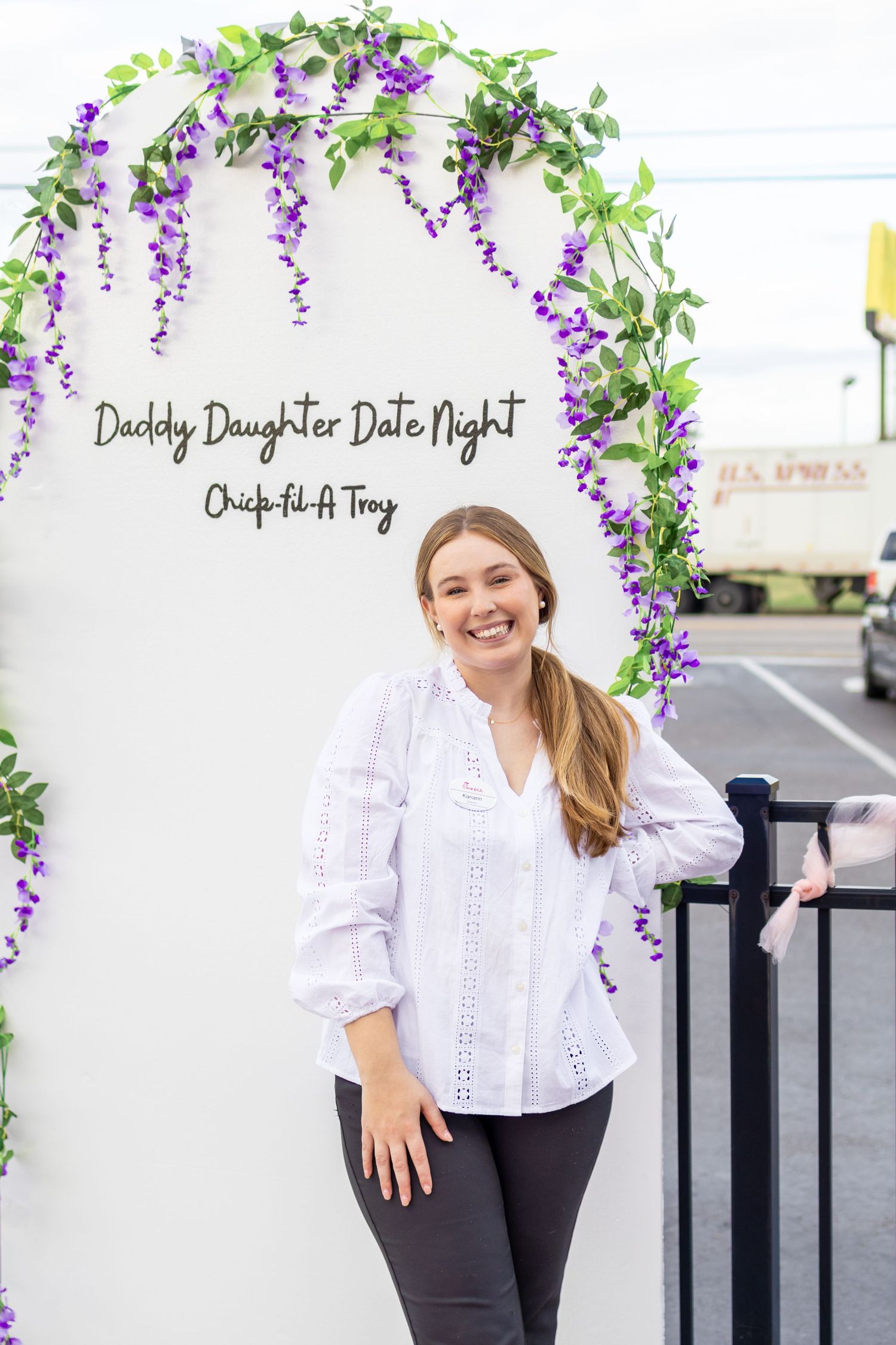 Professional outdoor portrait of someone wearing a white button-down shirt and black pants against a floral backdrop.