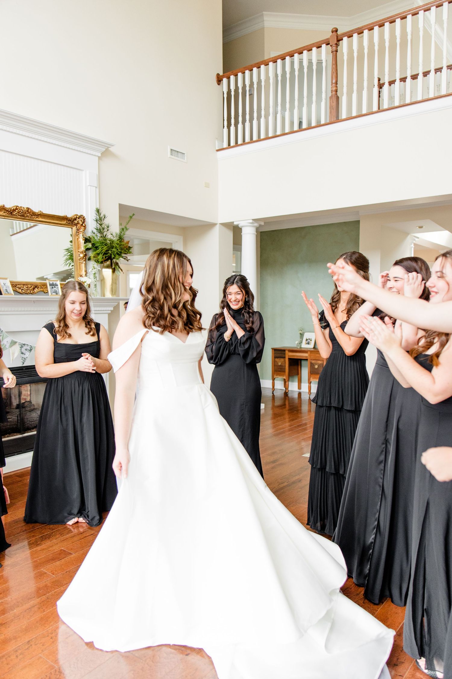 Wedding party gathered in elegant home interior with bridesmaids in black dresses admiring bride in classic white gown.