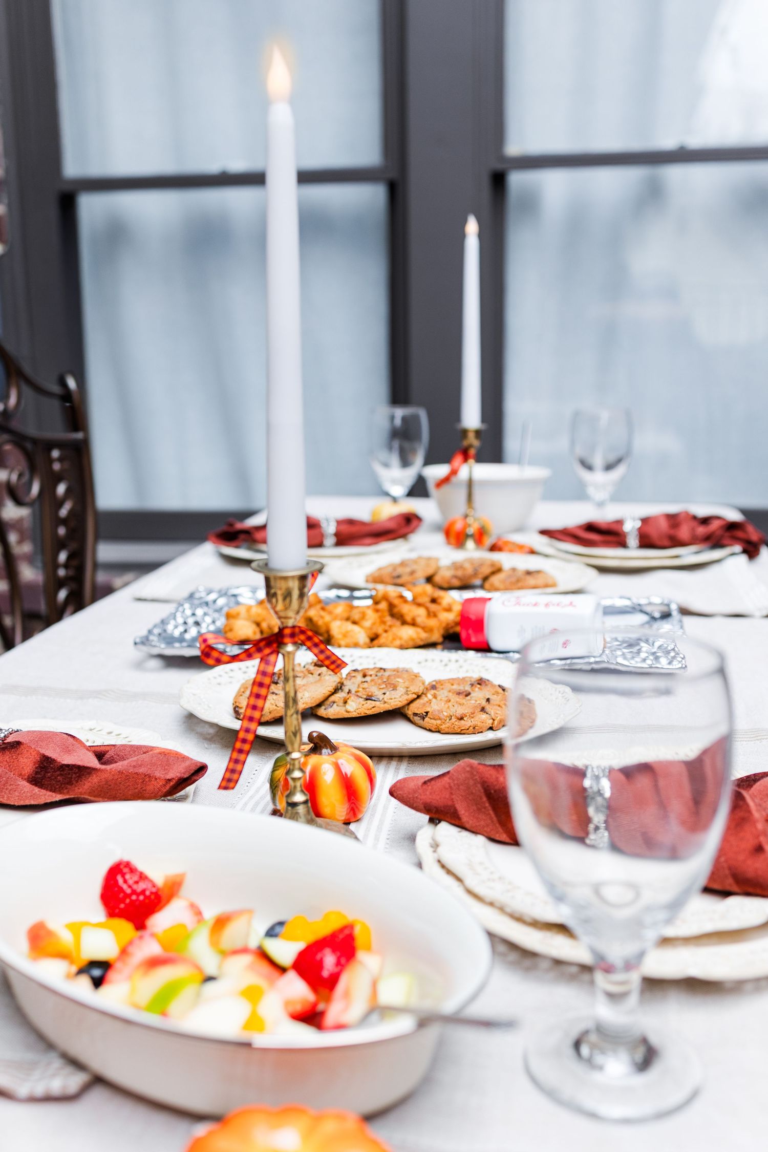 An elegant holiday table setting with white candles, red napkins, and a festive spread of food and wine glasses.
