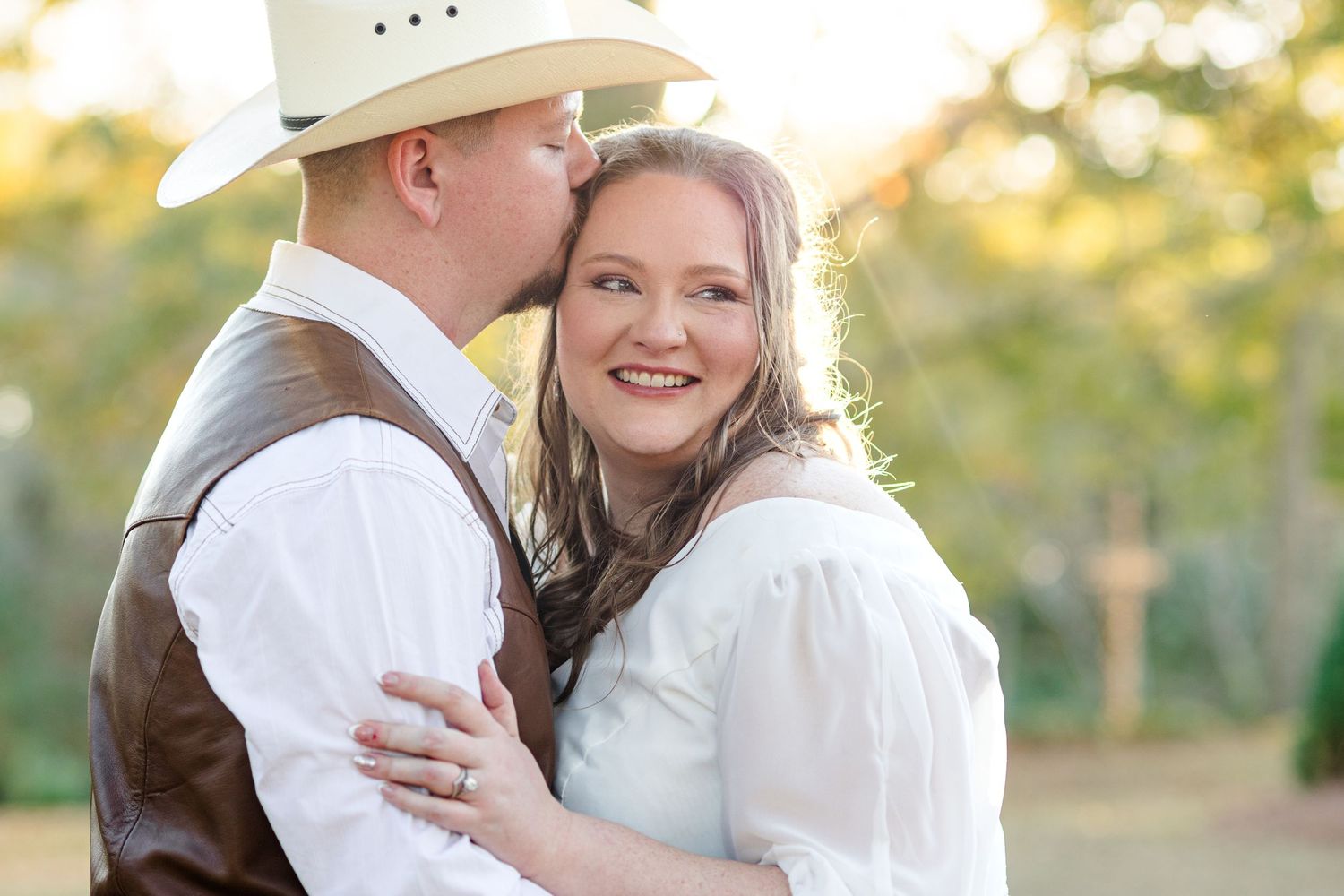 A couple in white outfits share a romantic moment during an outdoor sunset photo session.