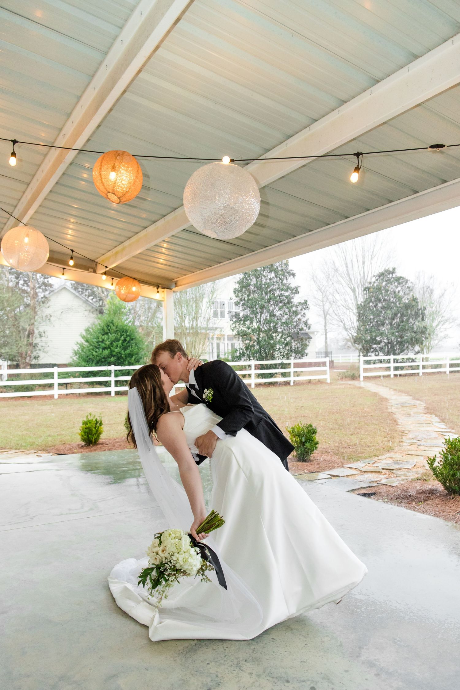 A romantic dance dip captured under a covered outdoor venue with paper lanterns and natural lighting.