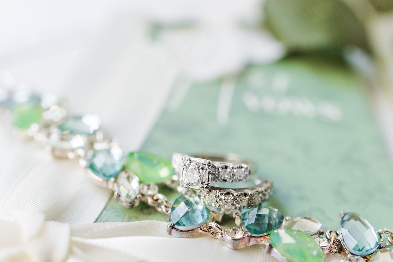 Delicate silver engagement rings with blue gemstones displayed on a mint green surface with scattered crystals.