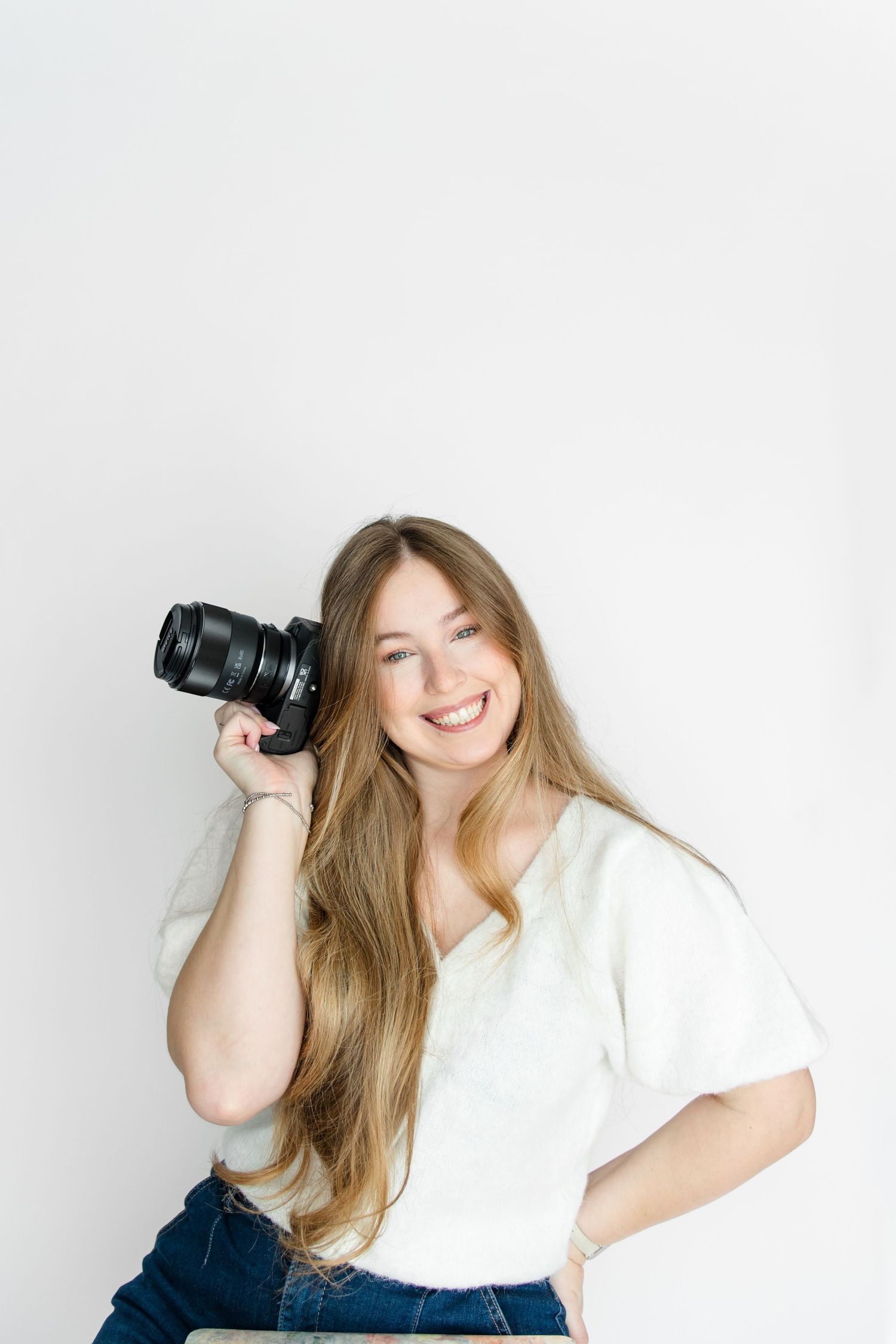 Professional photographer in white t-shirt and jeans holding DSLR camera against white background.