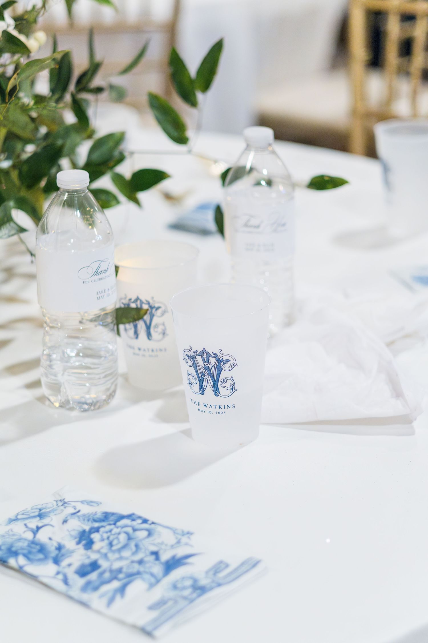 Elegant table setting with white linens, monogrammed water bottles and delicate blue floral details.