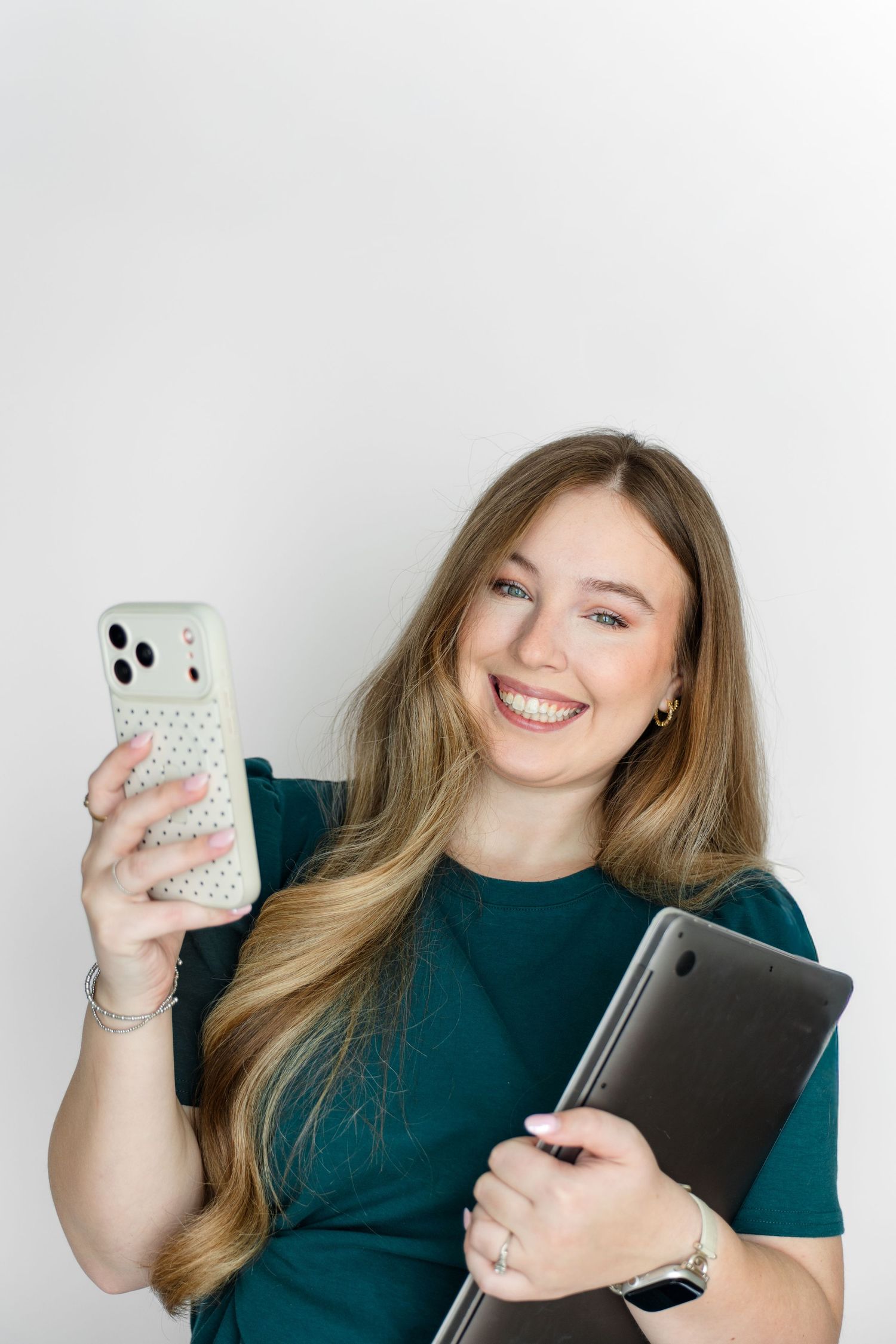 Person in dark shirt smiles while holding mobile phone and tablet against white background.