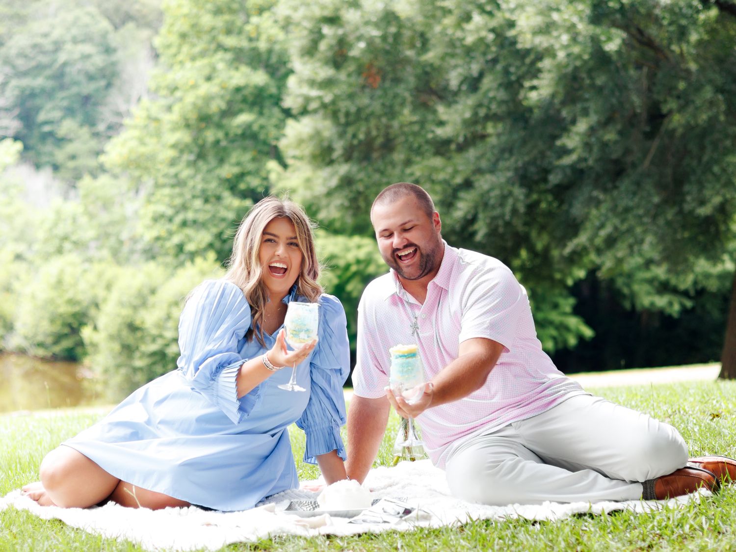 A couple in light casual clothing enjoys a romantic summer picnic on a blanket in a lush green park setting.