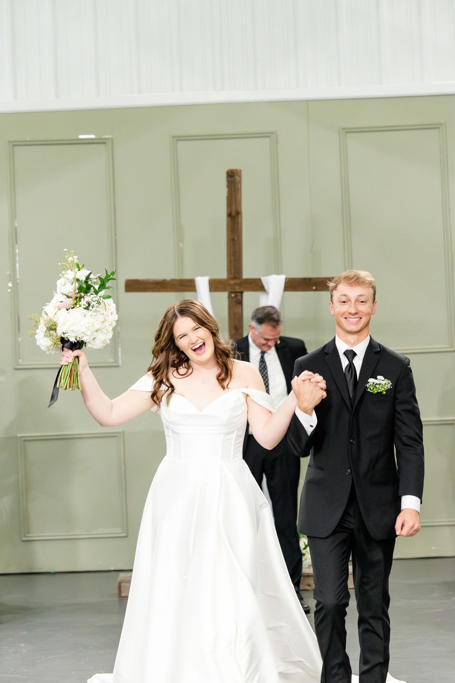 A wedding party walks and dances joyfully down a hallway with sage green paneled walls.