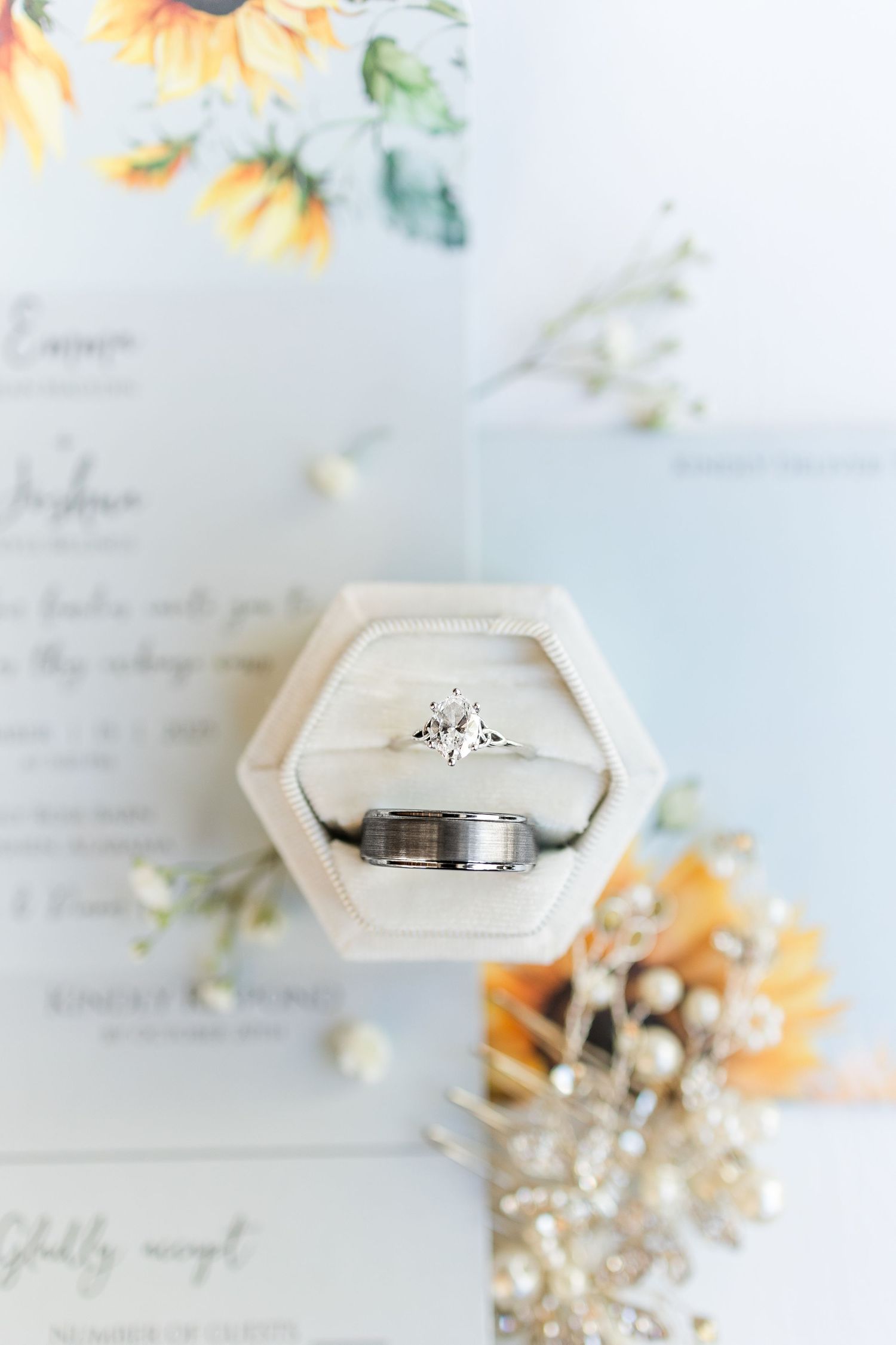 Wedding rings and delicate floral decorations arranged on a white surface with soft lighting.
