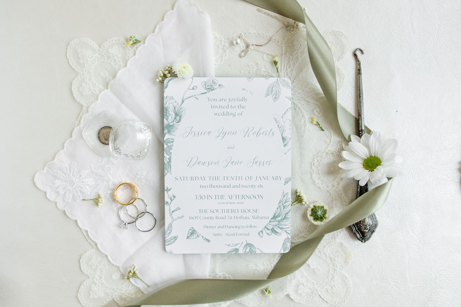 Wedding invitation suite with white daisies, rings, and delicate lace details arranged on a light background.