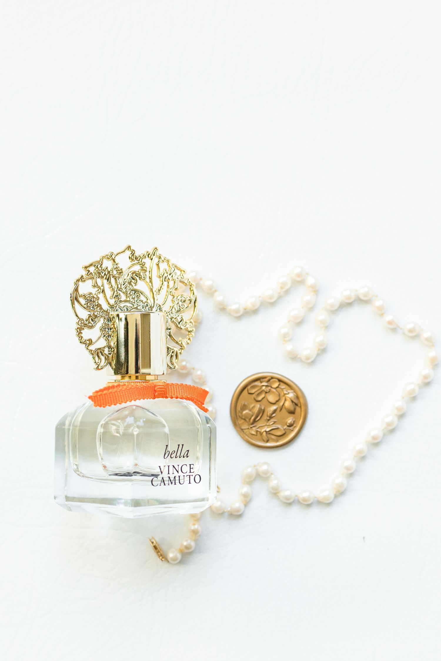 Elegant perfume bottles with gold ornate caps and pearl necklaces arranged on white background for luxury fragrance styling.