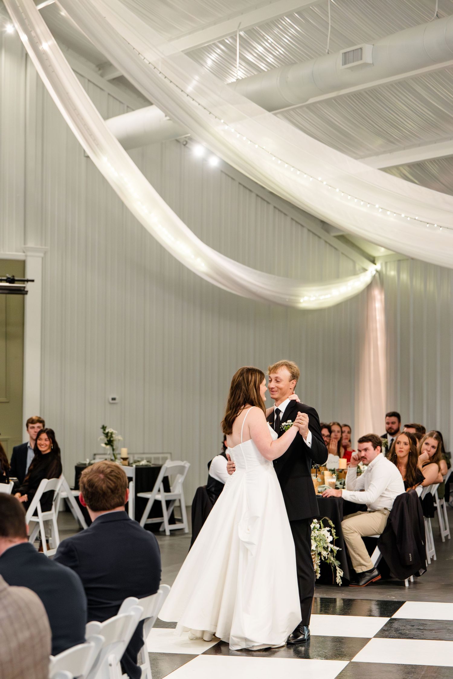 Wedding reception venue decorated with elegant white draping and guests seated at tables enjoying a formal dinner celebration.