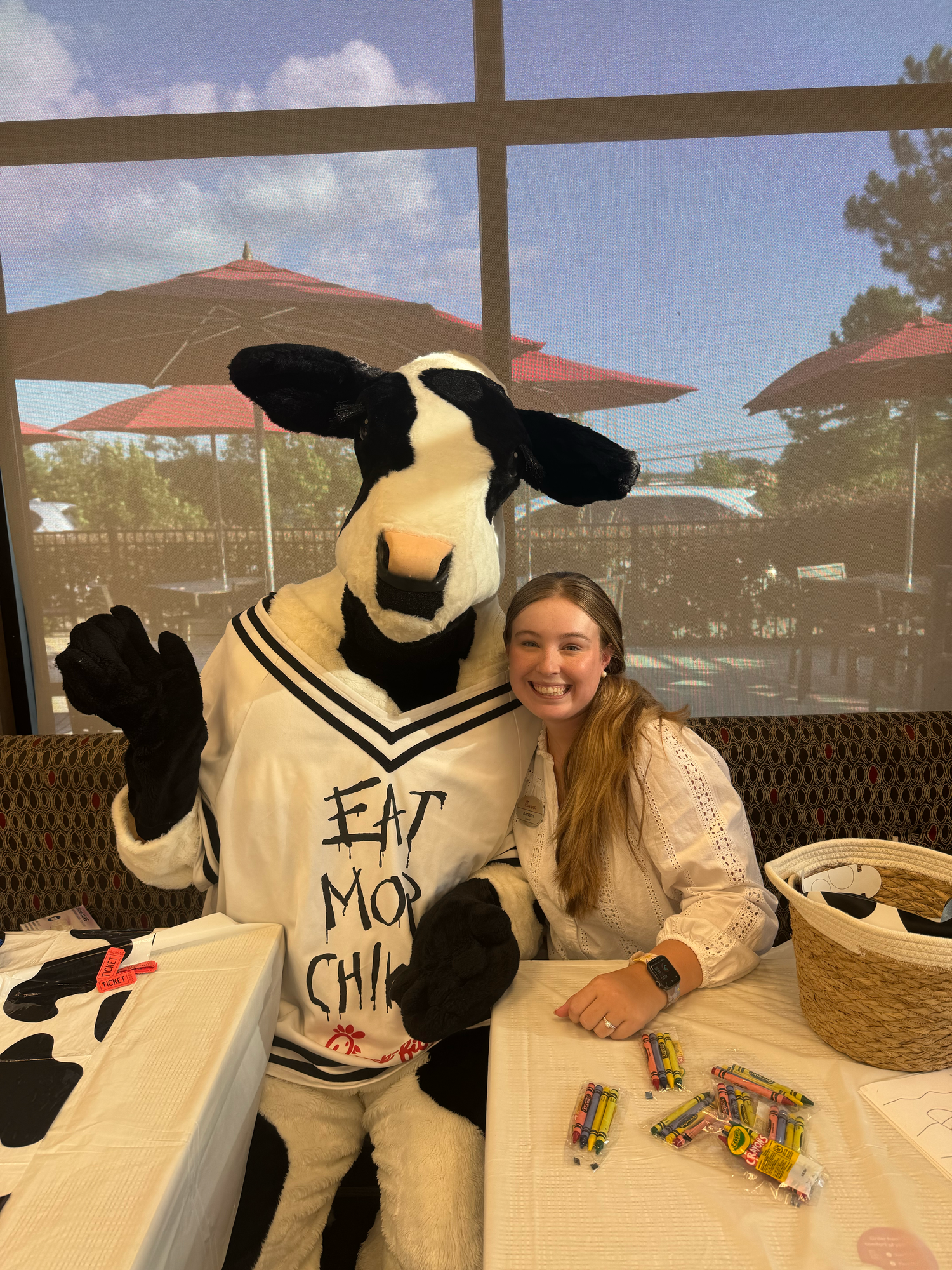 A person sits at an outdoor restaurant table with a large plush cow mascot character in multiple sequential photos.