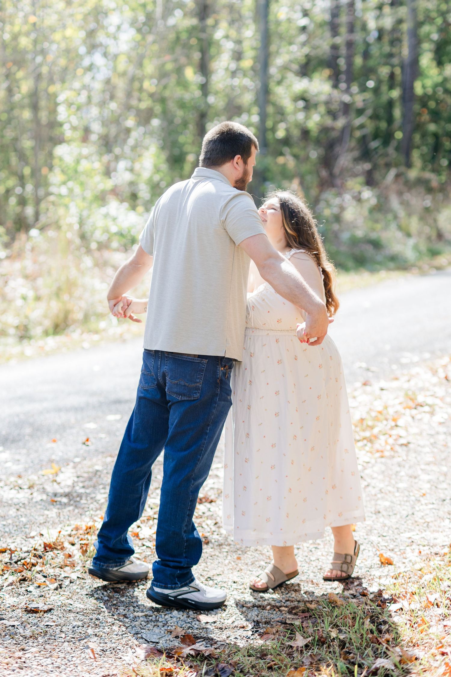 A couple in casual attire walks together on a leaf-covered path in an autumn forest setting.