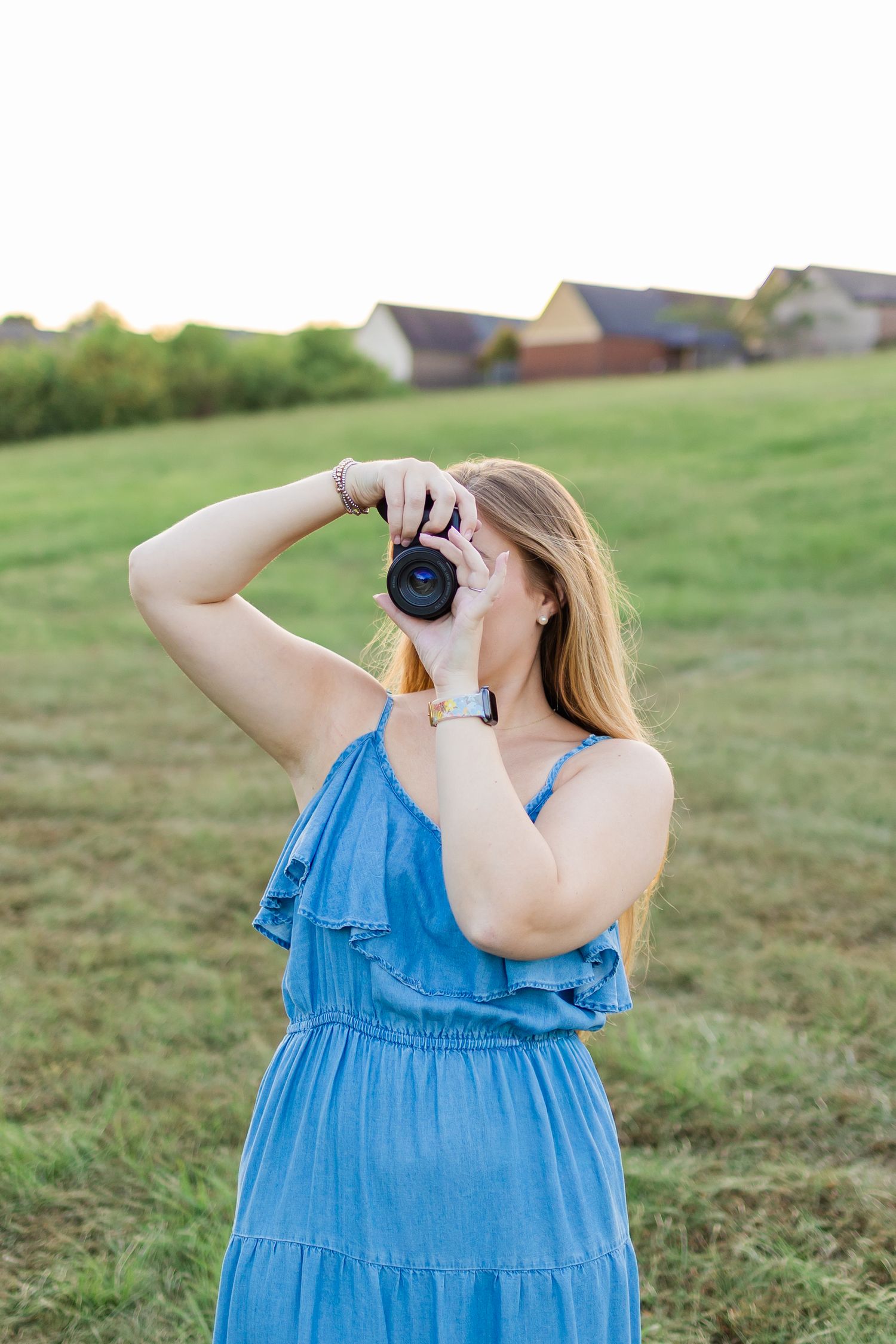 A person in a blue ruffled sundress holding binoculars to observe nature in a grassy field.