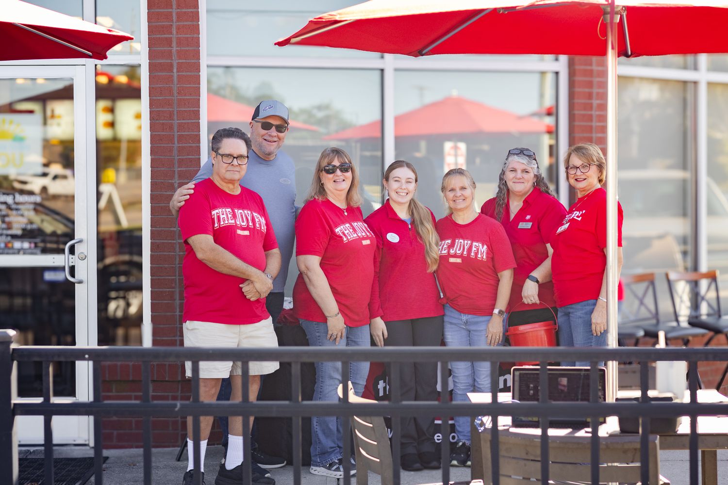 A row of red patio umbrellas shade outdoor seating at a restaurant with customers visible in the background.