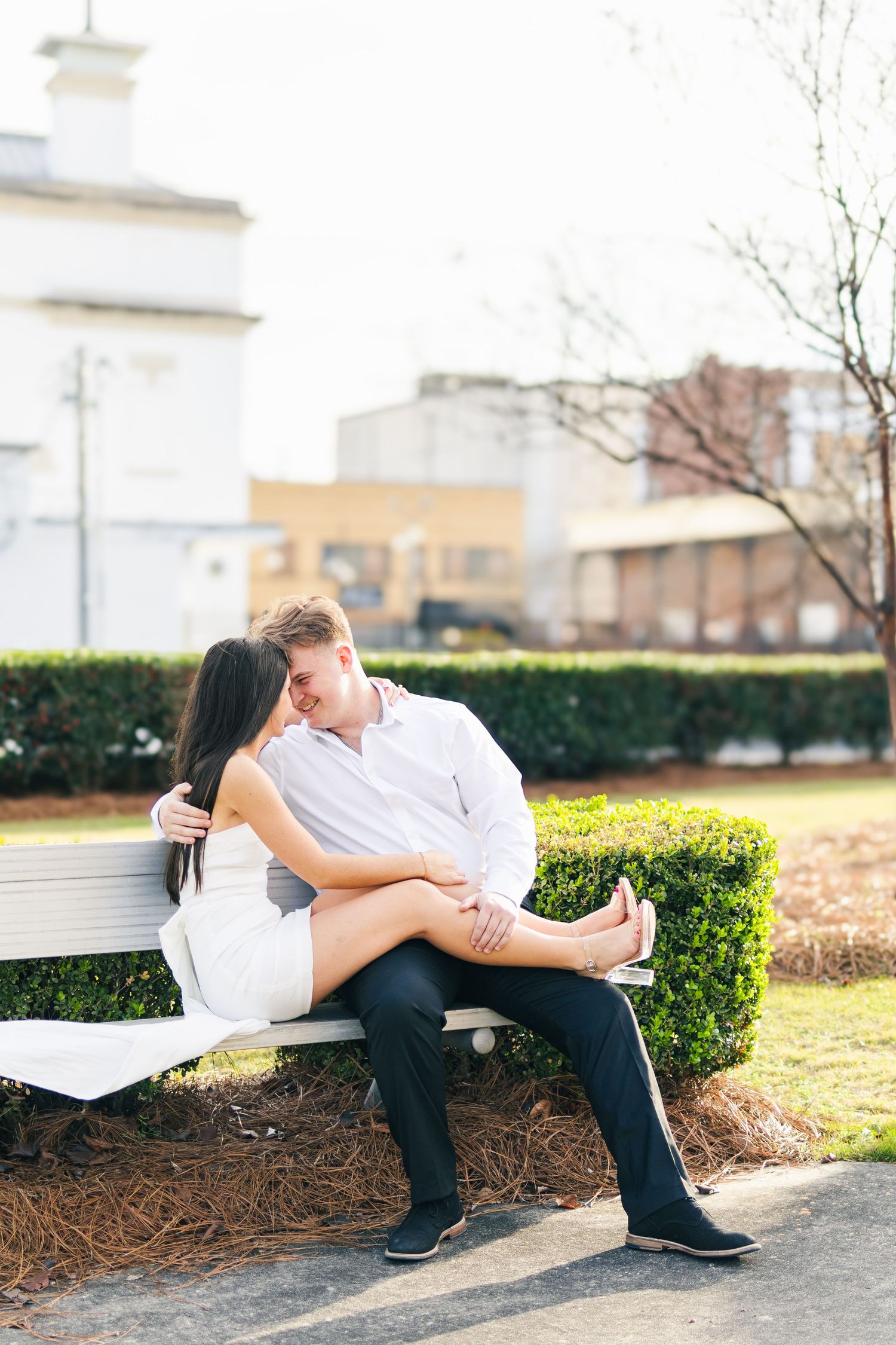 Romantic couple in white and black attire sharing intimate moments on a bench in a garden setting.