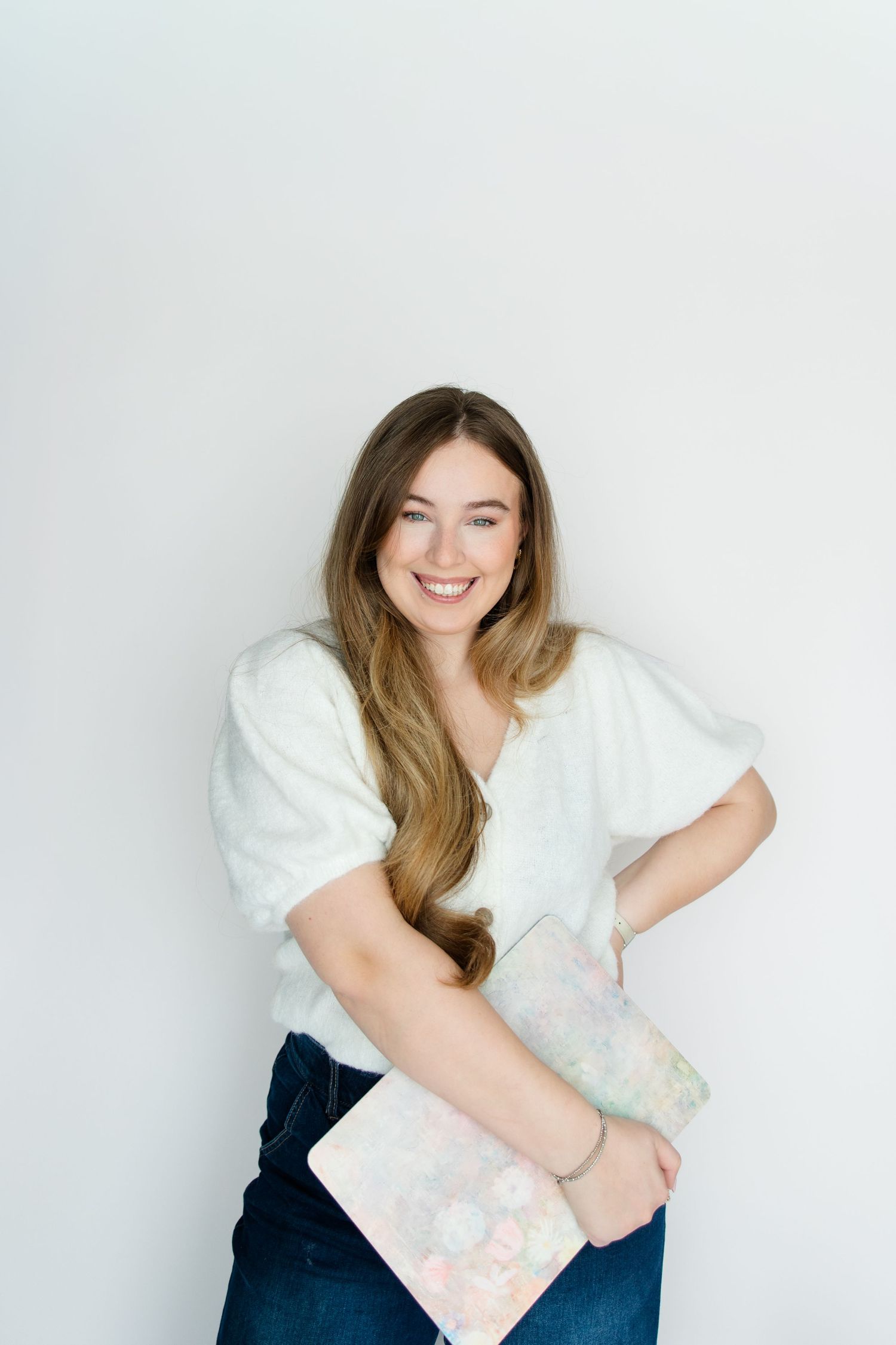 A person in a white top and dark pants poses casually against a light background in a lifestyle photoshoot.