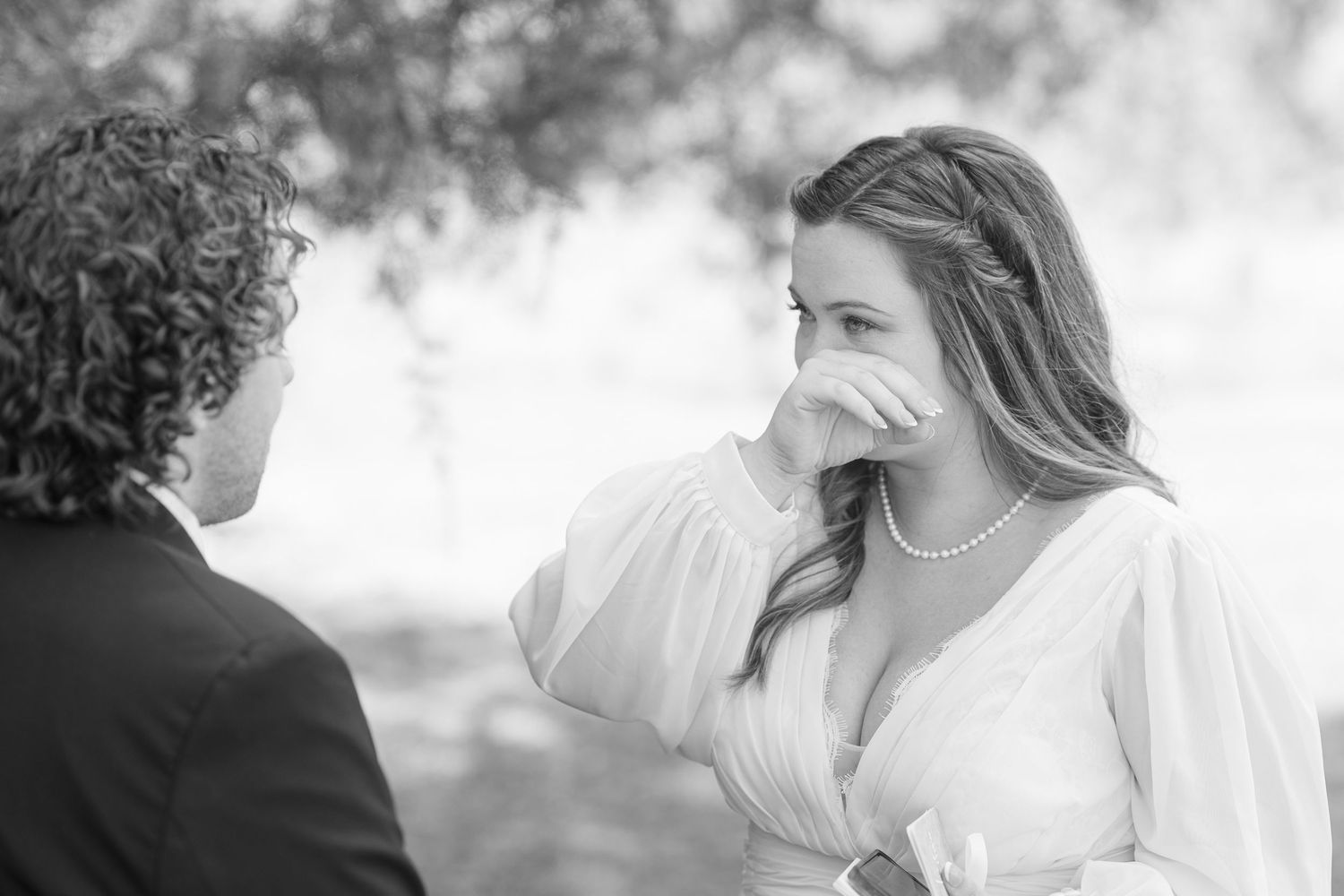 Black and white photo of an emotional wedding moment outdoors with bride in flowing white dress.