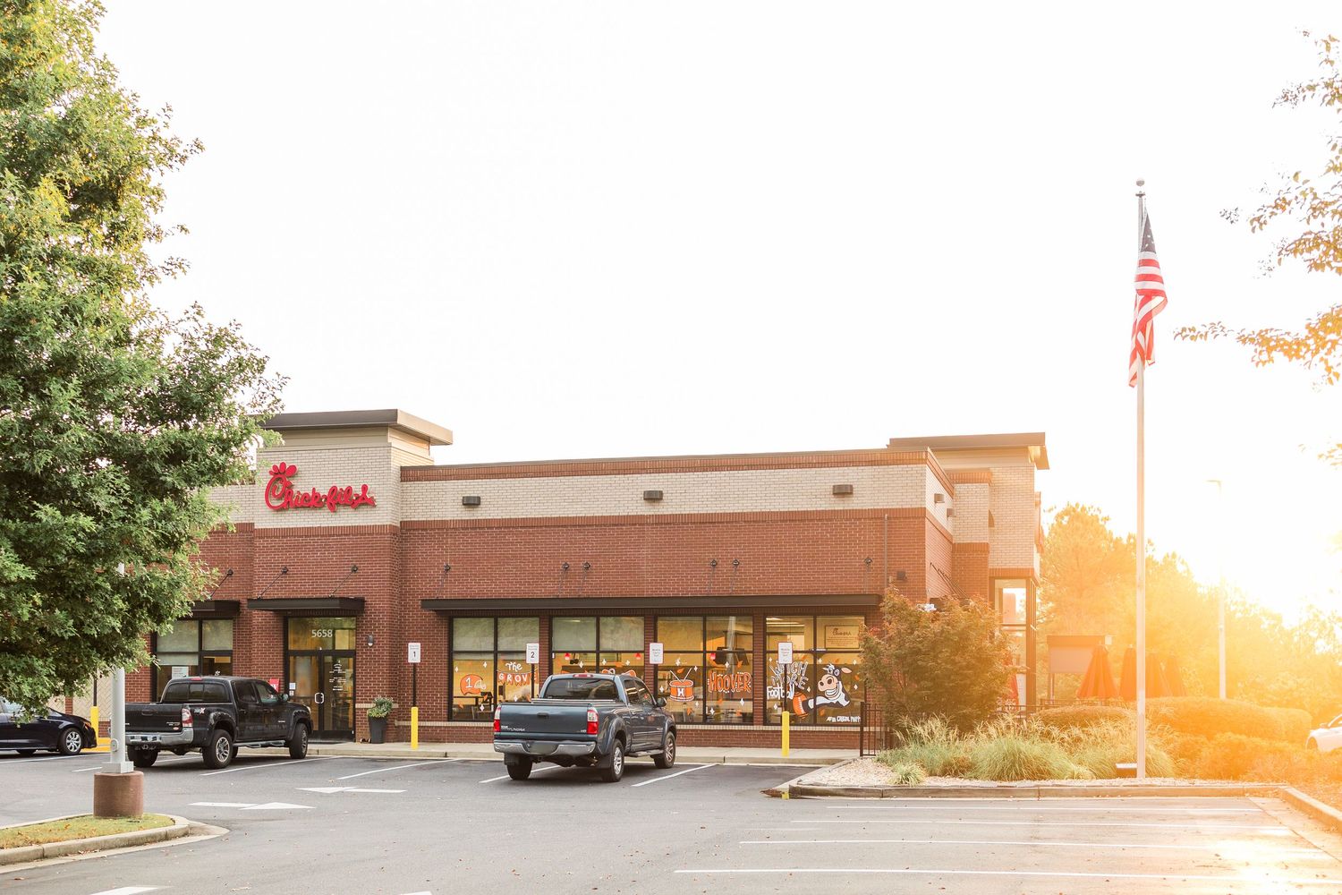 Exterior view of a strip mall with multiple retail storefronts and parked cars during golden hour sunset.