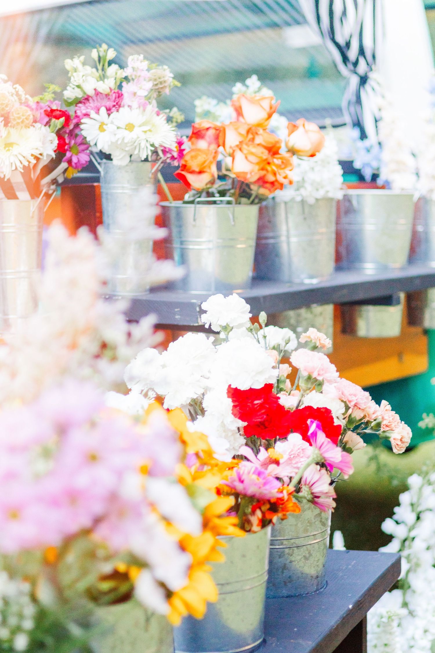Colorful daisies and flowers arranged in metallic buckets on display shelves in soft dreamy lighting.