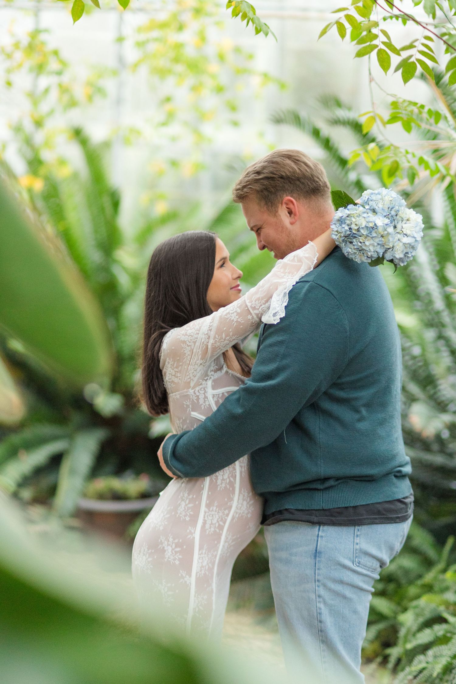 A couple embraces lovingly in a lush garden setting with soft natural lighting and green foliage in the background.