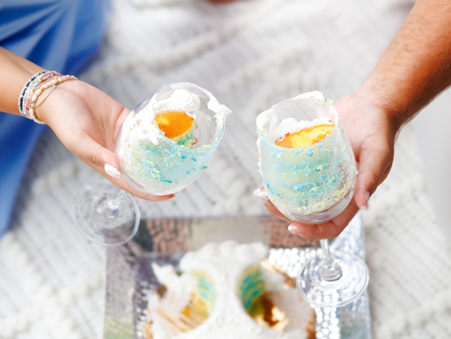 Two glasses of blue cocktails with orange citrus garnish being held during a toast at a celebration.