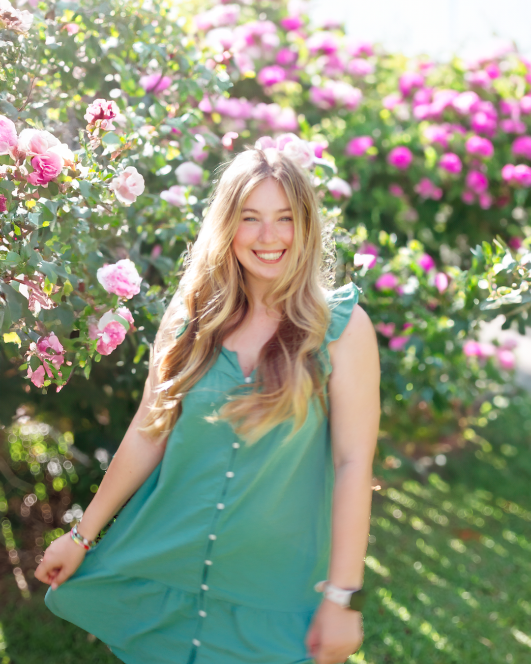 Figure in a green sleeveless dress twirls and smiles among blooming pink roses in a sunny garden setting.