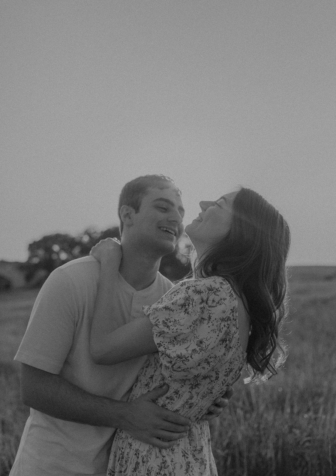 Couple sharing an intimate embrace and laughing together in a sunlit field.