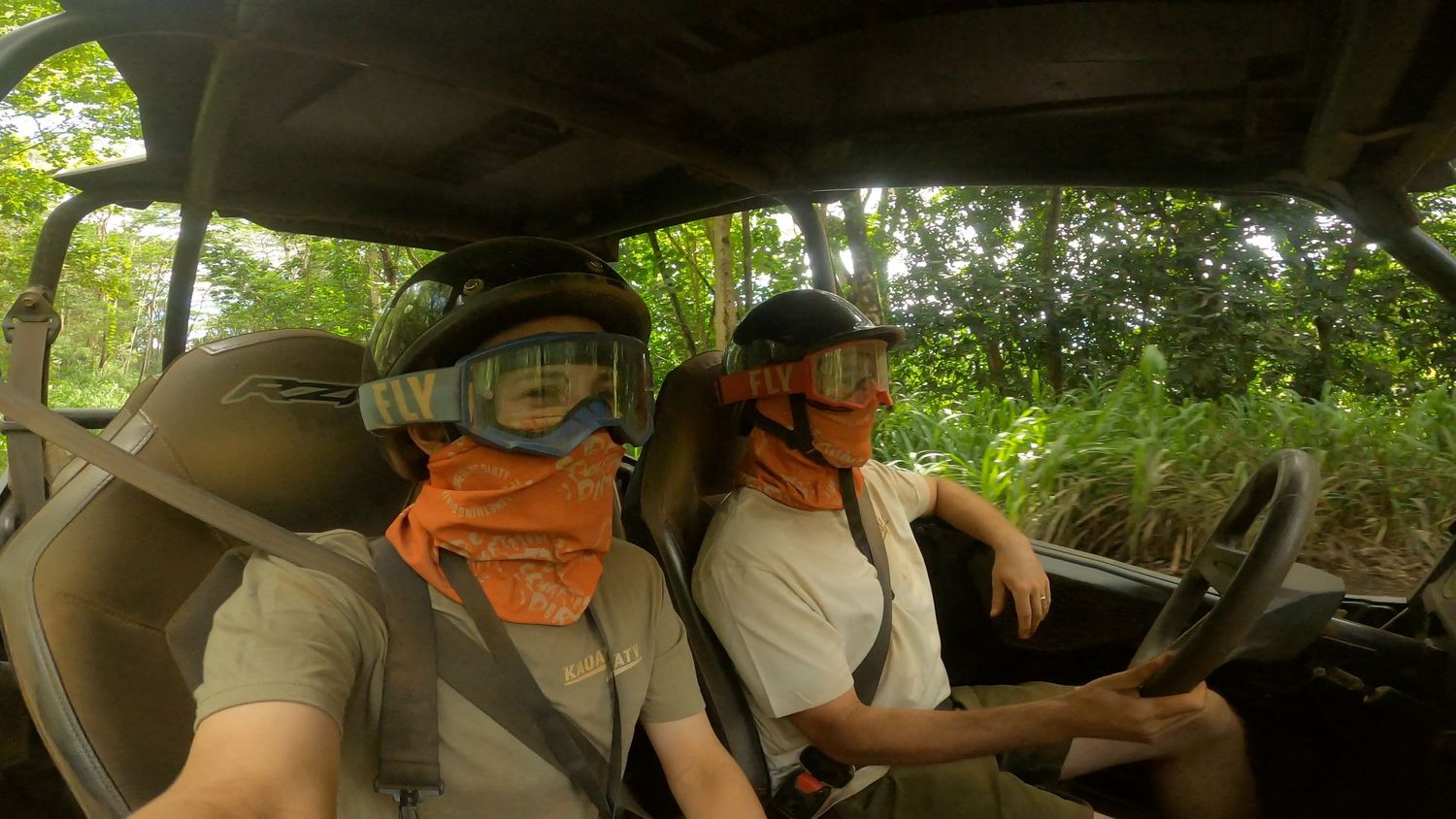Two people wearing protective gear sit in an off-road vehicle during a forest adventure.