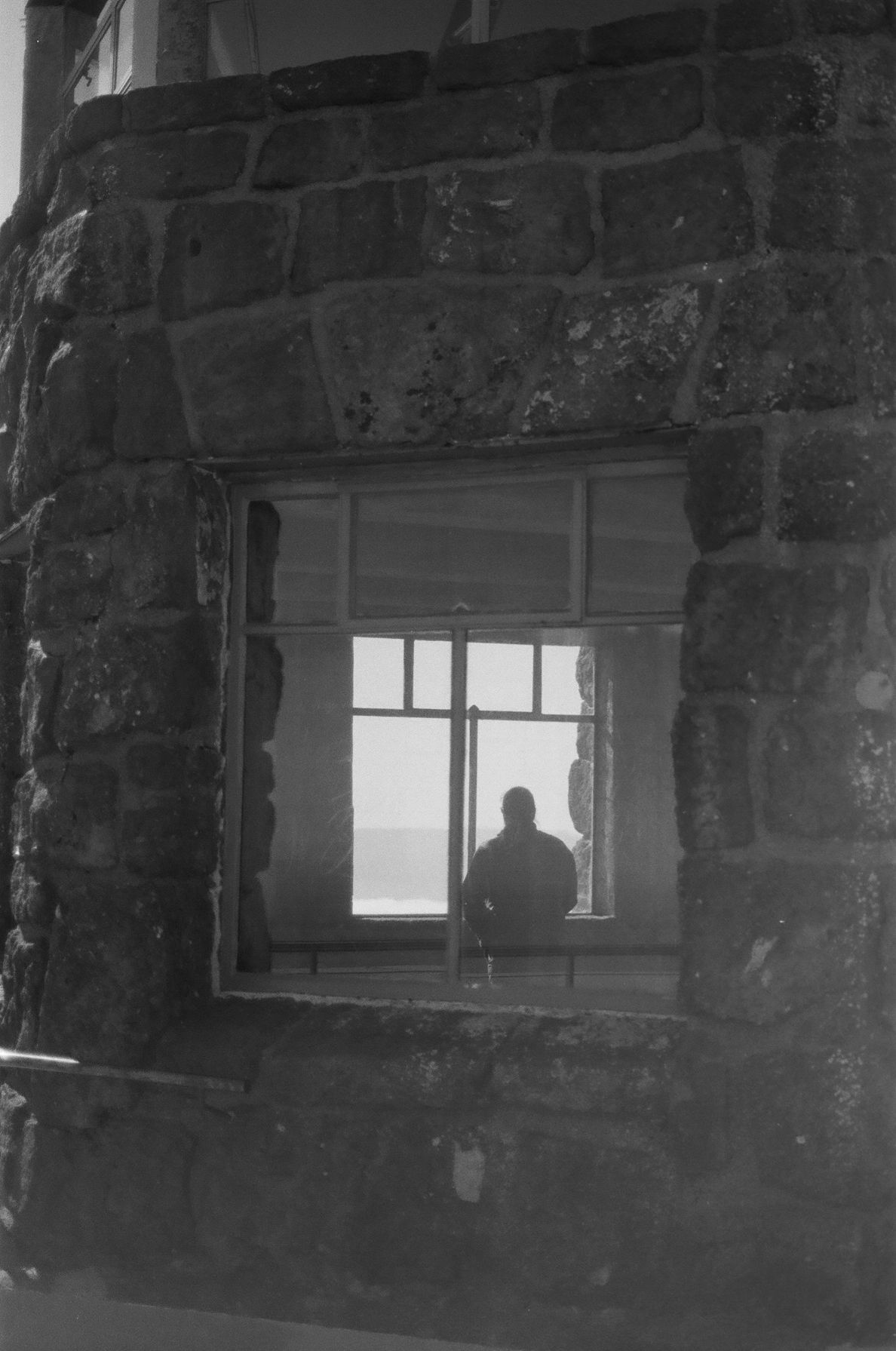 Black and white photo of a silhouetted person sitting by a window in a rustic stone building.