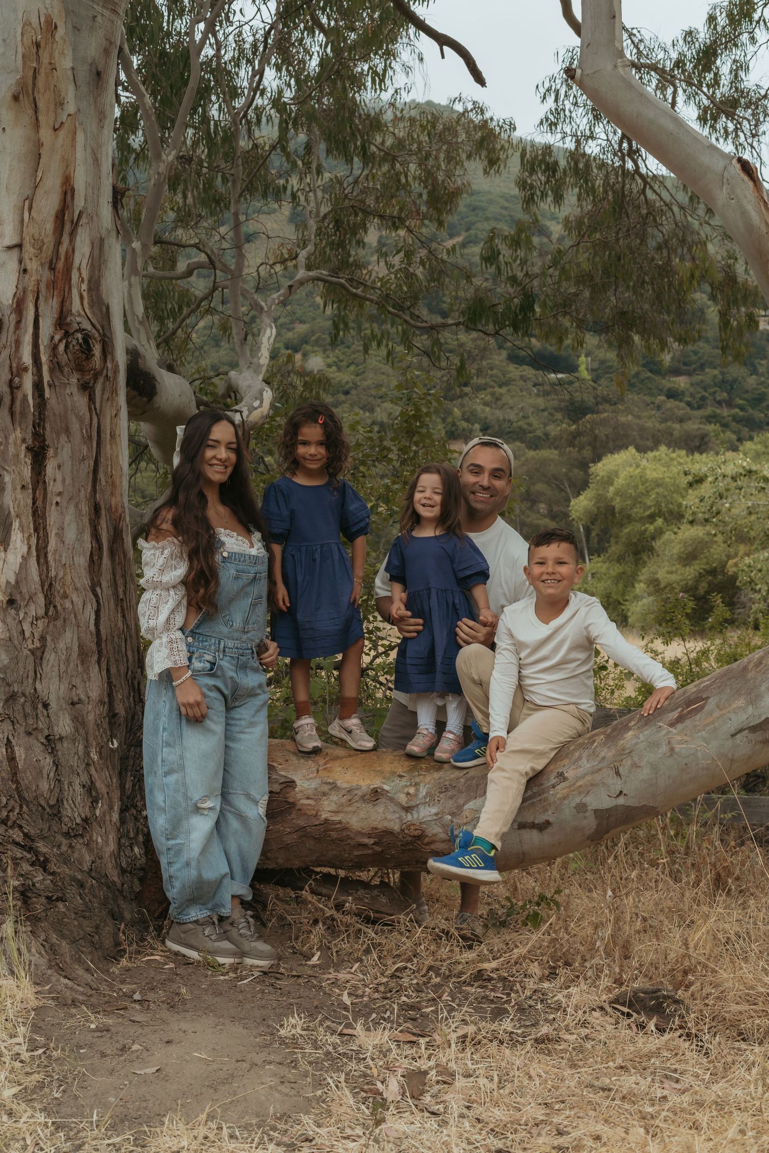Family sits together on a fallen tree trunk in a eucalyptus forest along a nature trail during a sunny day.