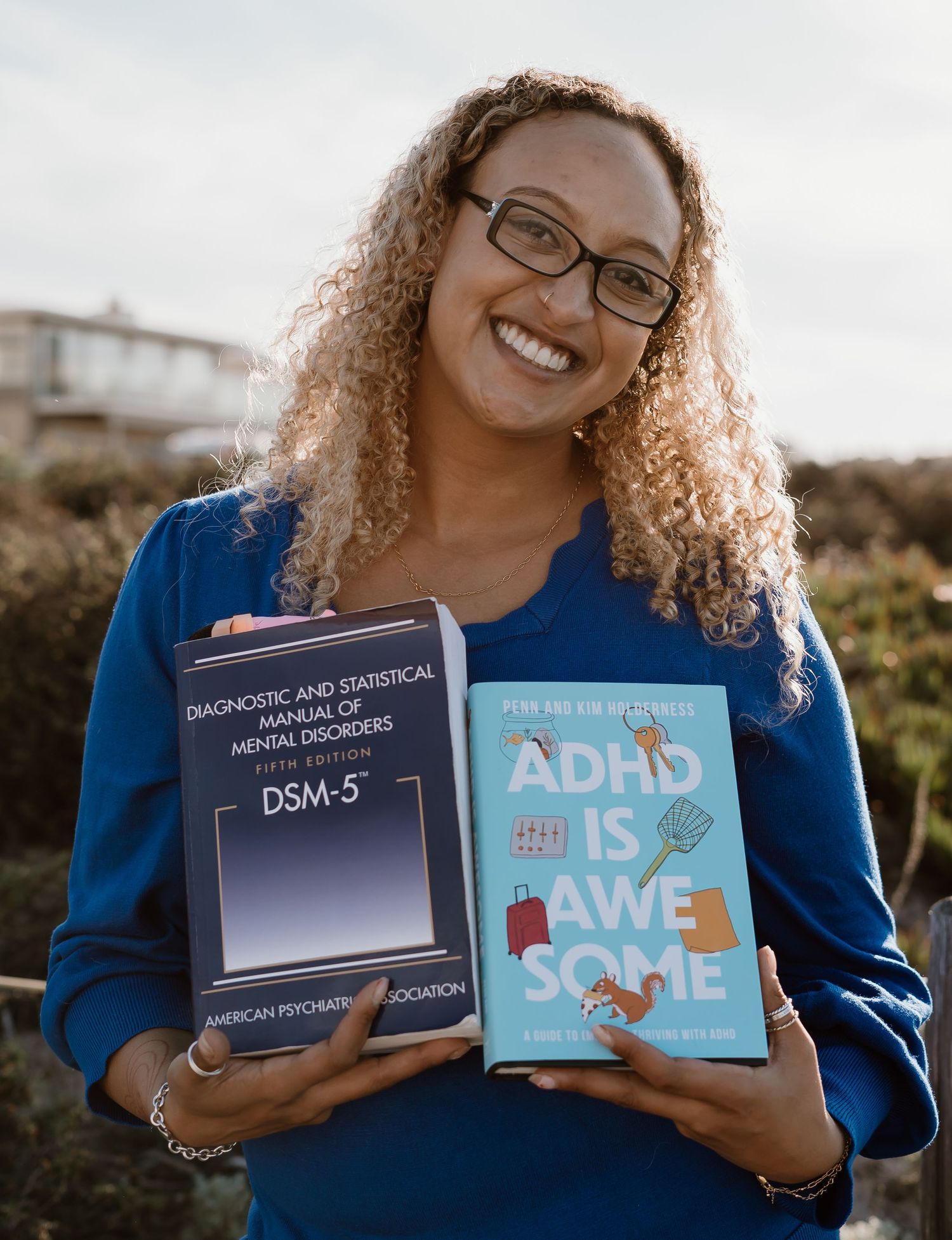 Someone holds up and displays two books about ADHD and DSM-5 diagnostic manuals while wearing a blue top outdoors.