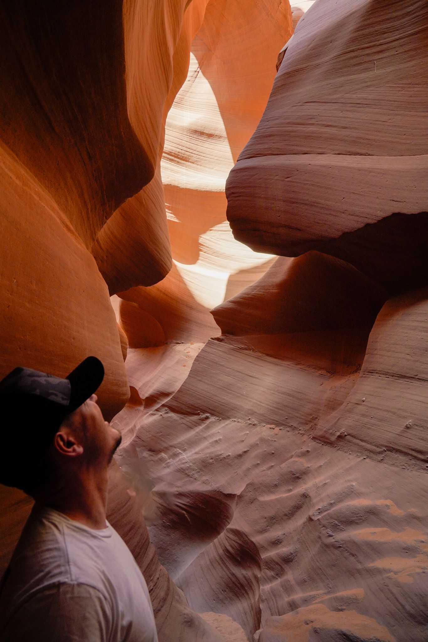 Man in black cap gazes up at the glowing orange sandstone walls of Antelope Canyon, Arizona.