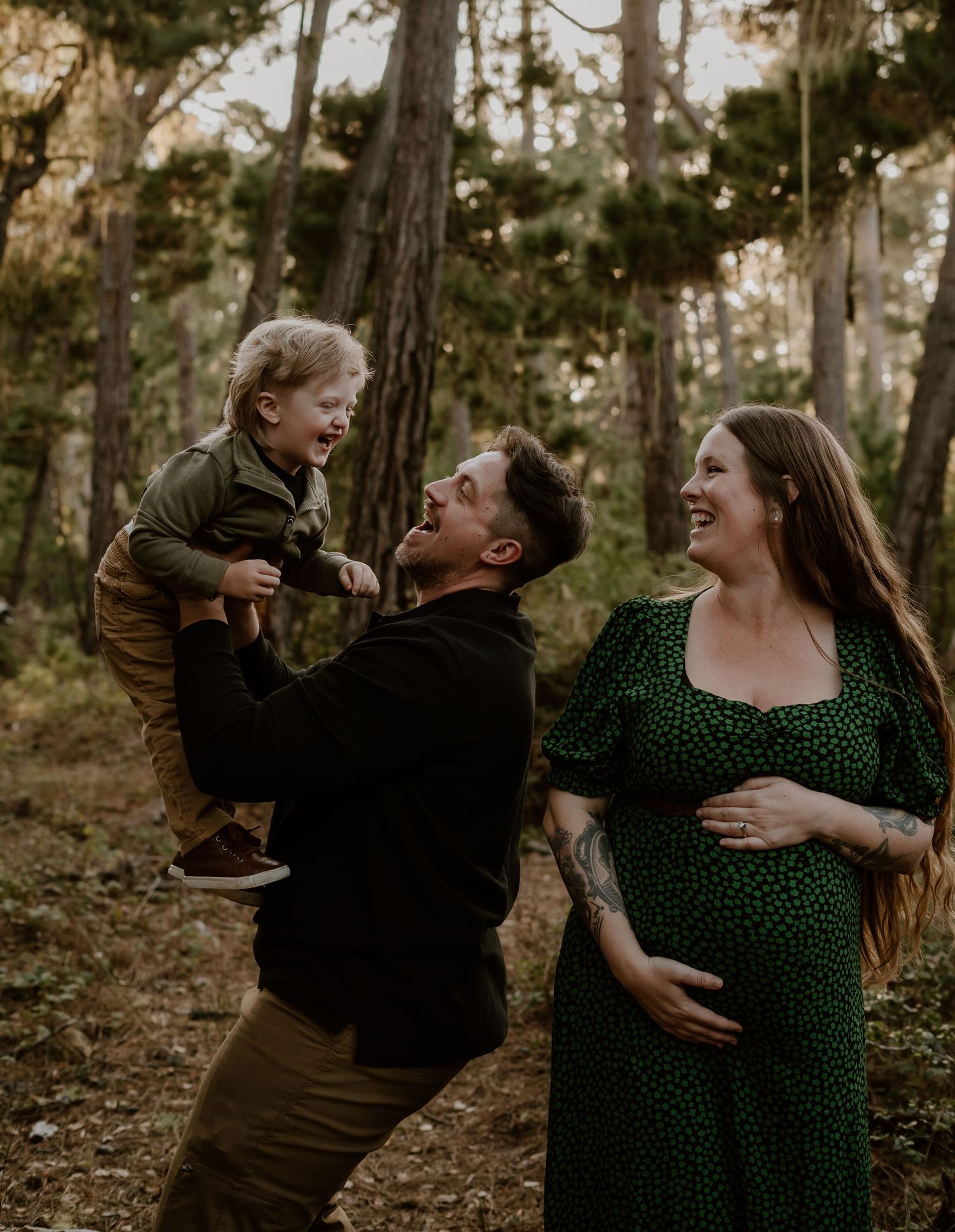 A joyful family moment captured in a forest setting with a small child and expectant mother in a green polka dot dress.
