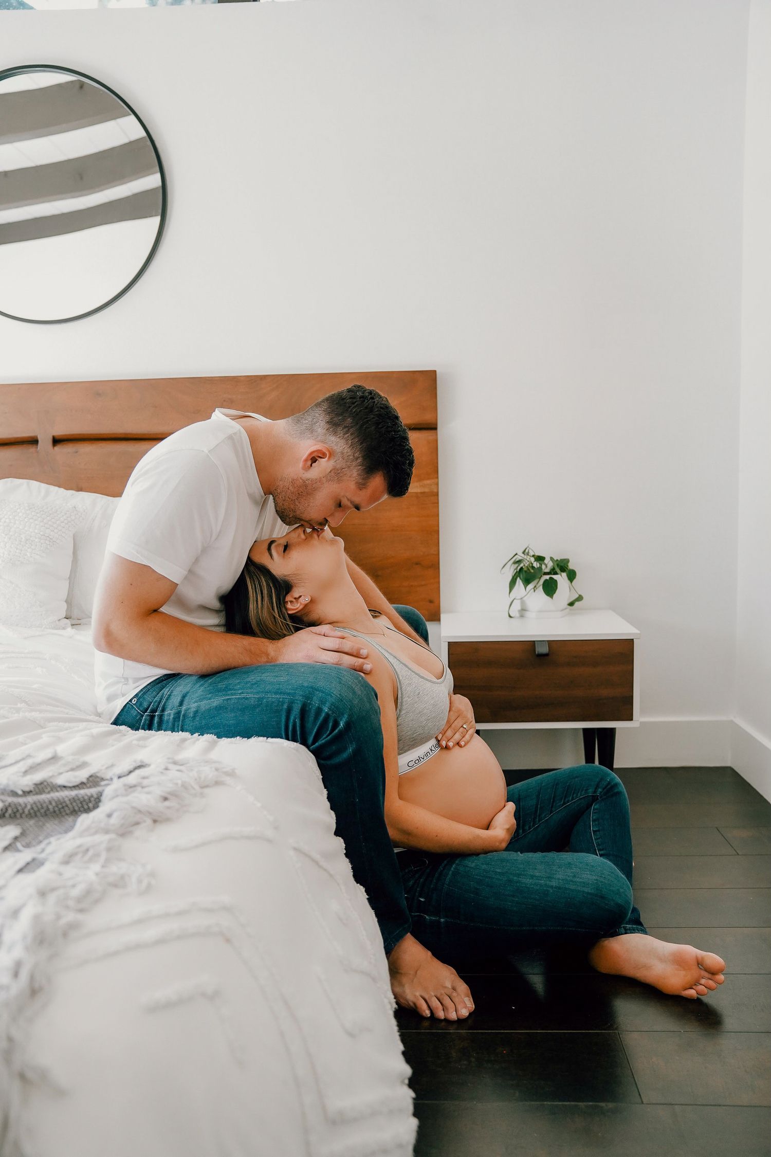 Intimate maternity photo of couple sharing tender moment on bed in modern bedroom.