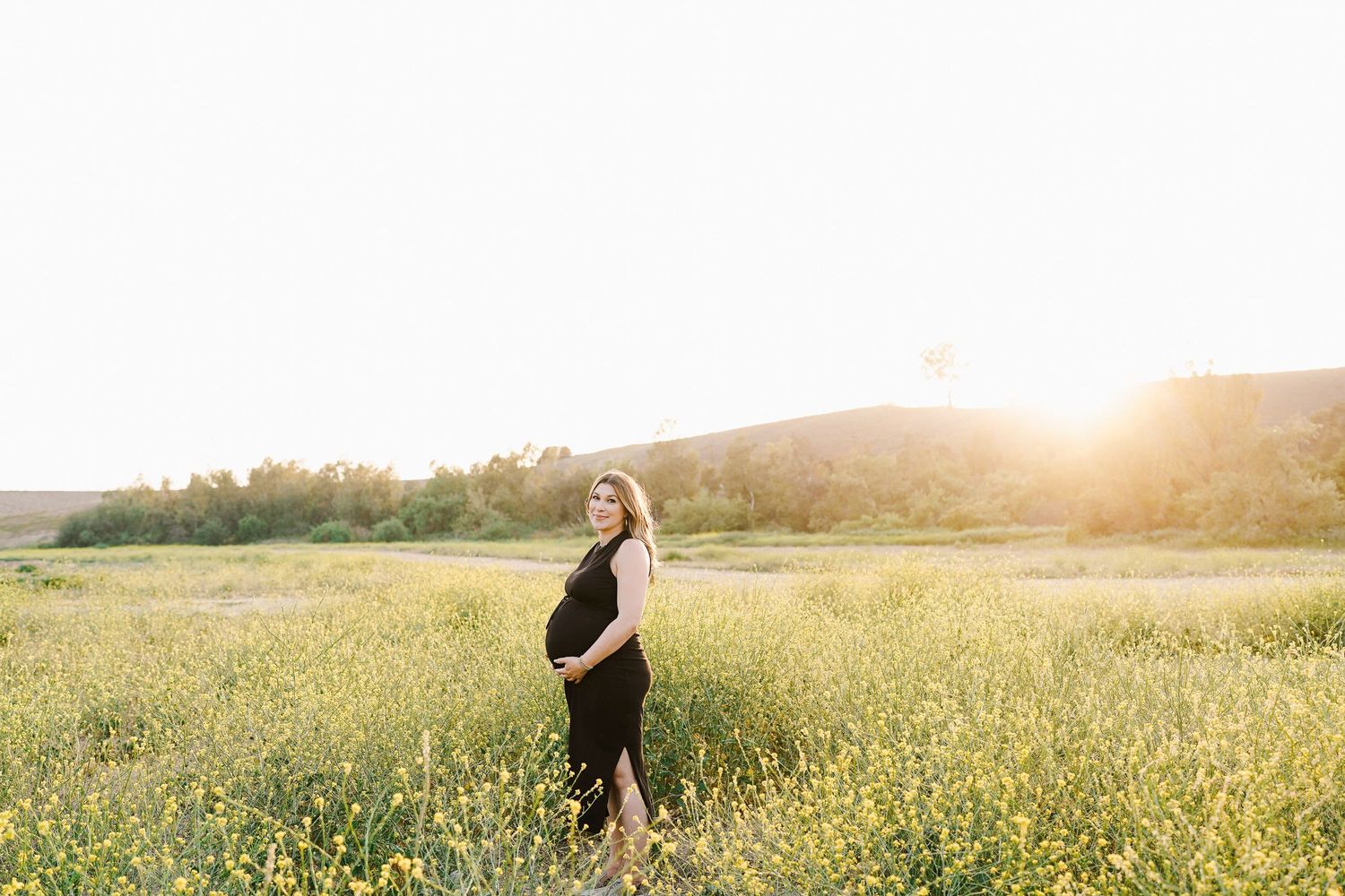 Silhouette of pregnant woman standing in golden wildflower field at sunset.