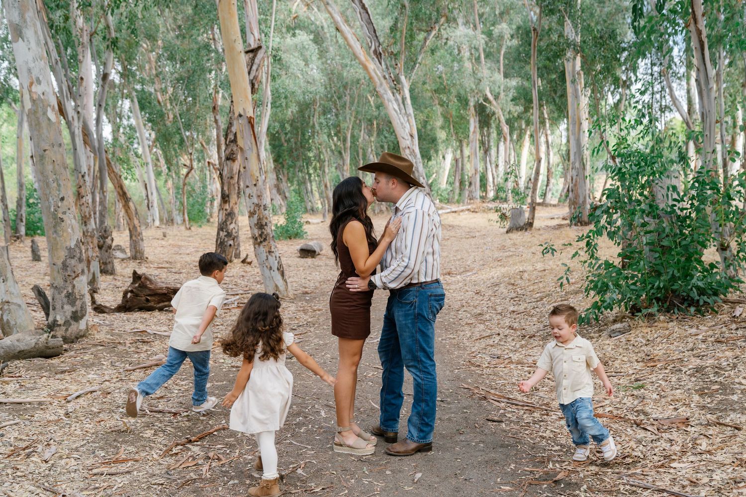 Family of five sharing a romantic moment on a forest path surrounded by eucalyptus trees.