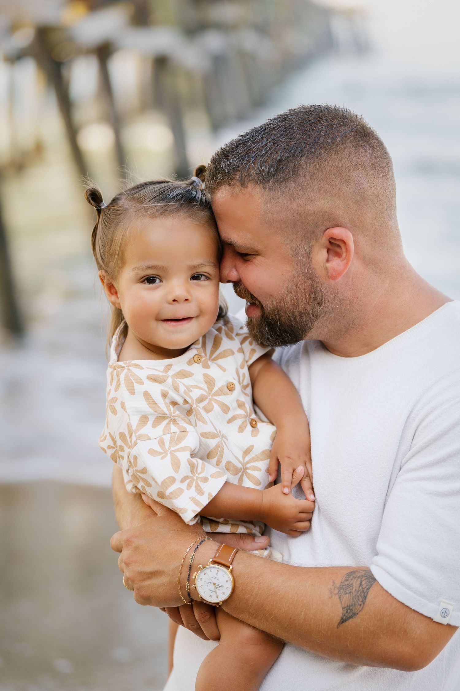 Tender moment between father and toddler by beach pier.