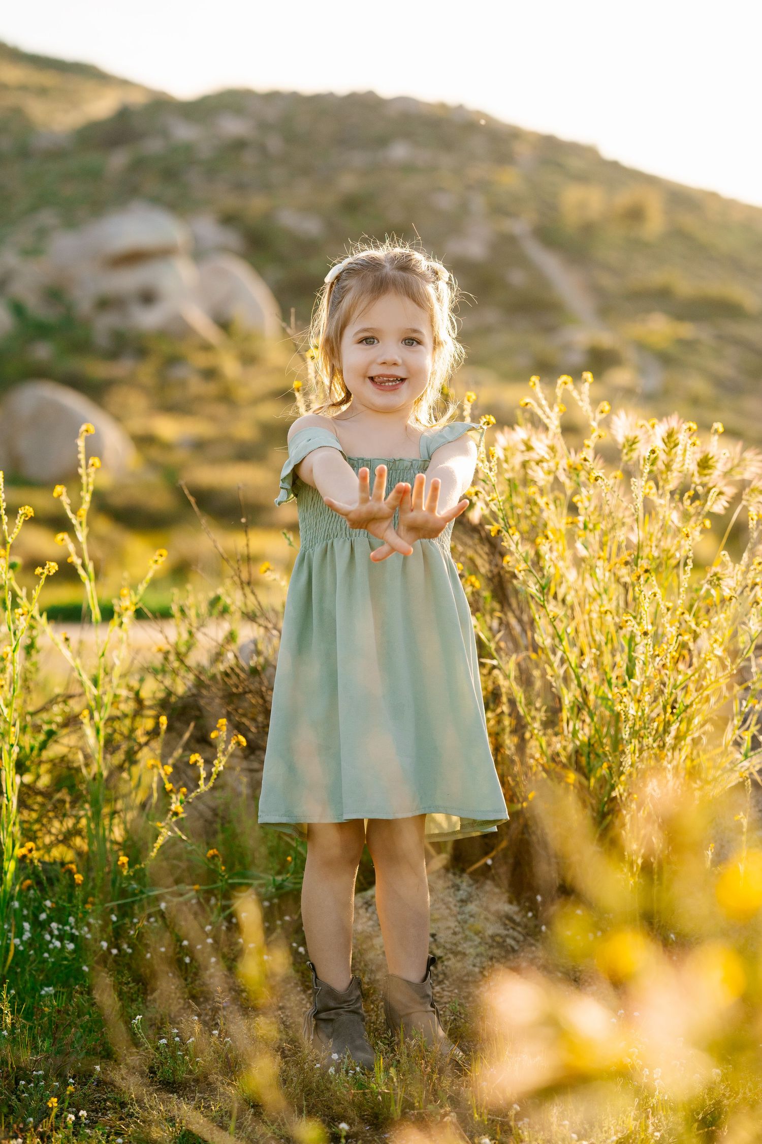 Child in mint dress playing among wildflowers during golden hour.