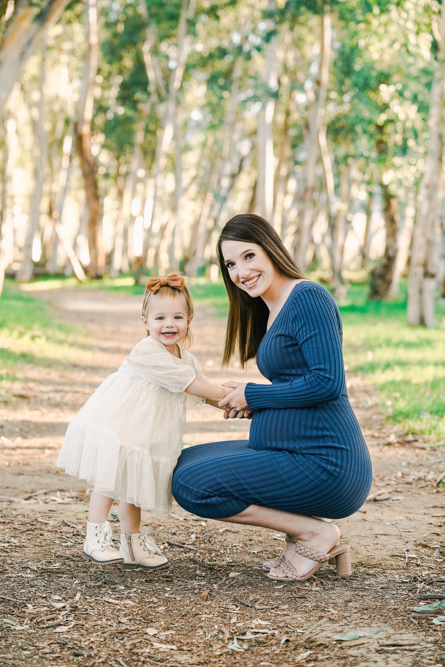 Mother and toddler share joyful moment on tree-lined path during autumn.